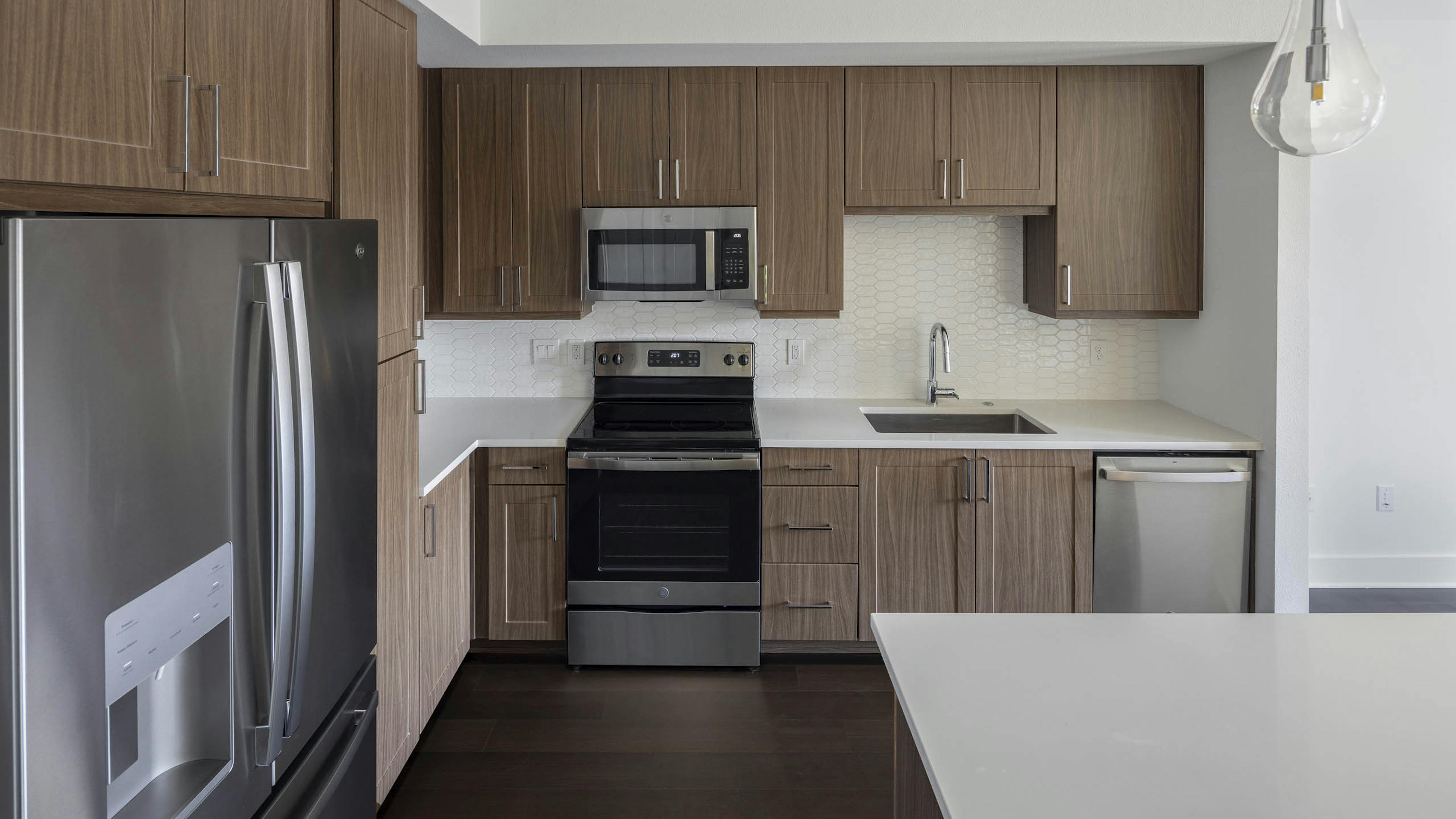 Close up view of AMLI Branch Park modern brown apartment kitchen cabinetry with dark flooring and sleek quartz countertops