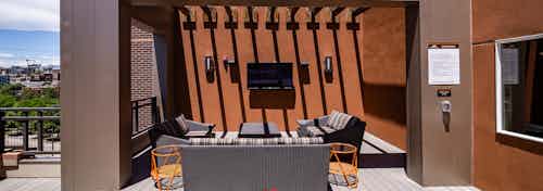 Exterior view of a rooftop living room at AMLI Riverfront Park apartments featuring a couch and chairs with a television