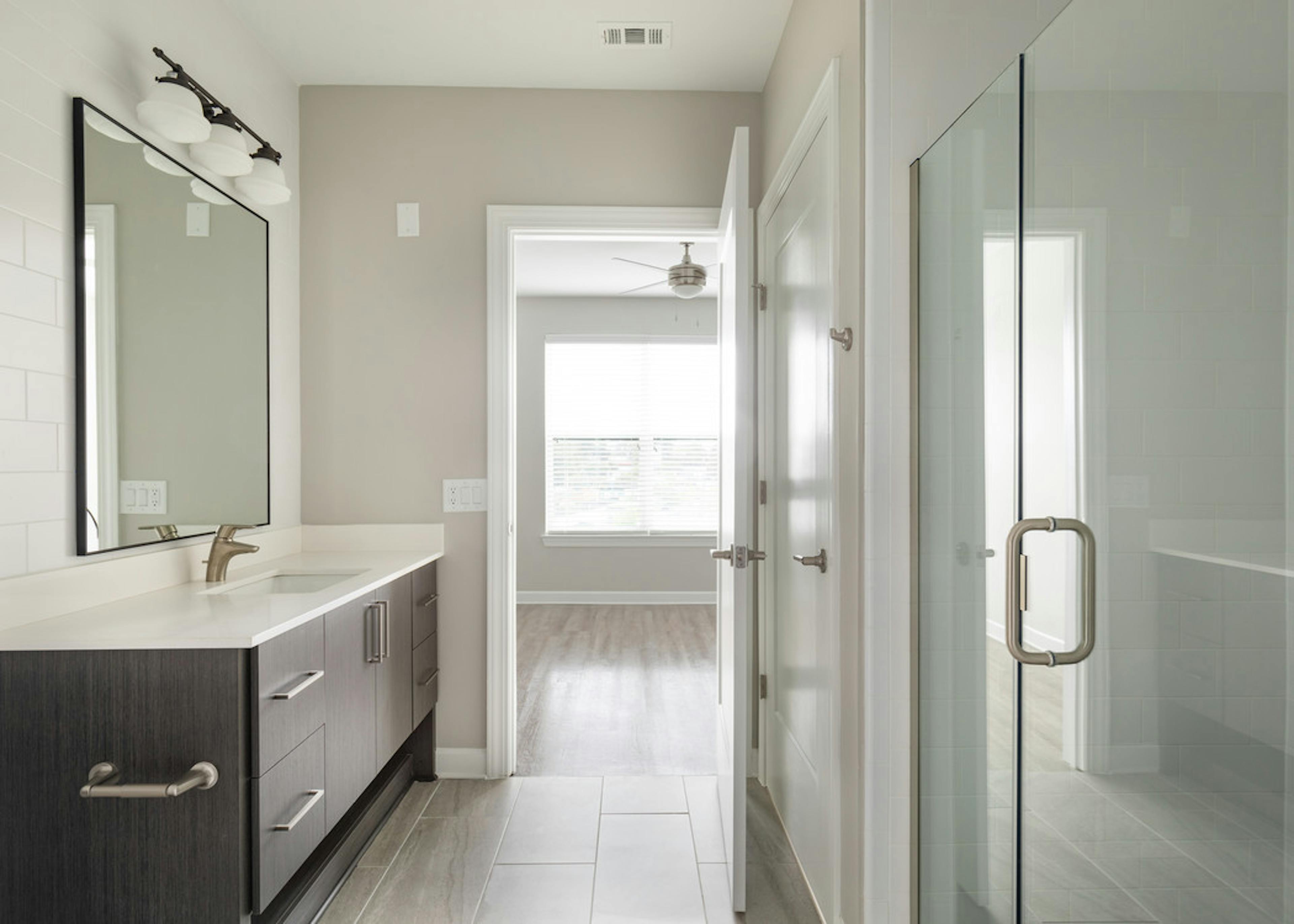 AMLI Westside bathroom with dark wood cabinets and a single sink with stand up shower and door peeking into hardwood bedroom