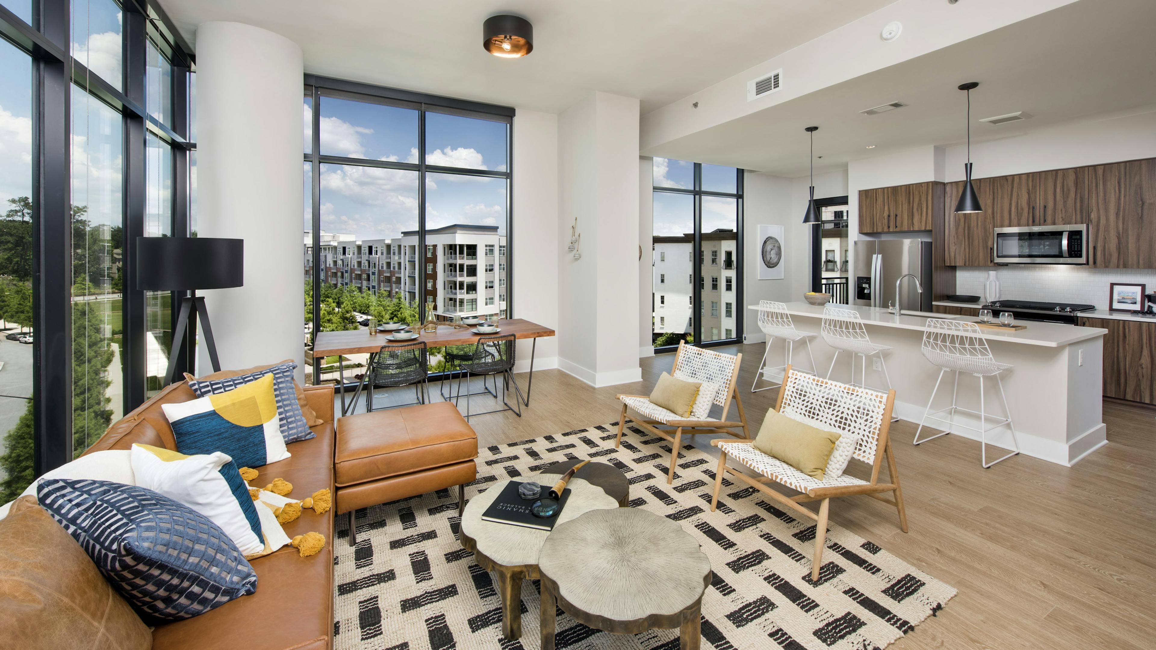AMLI Lenox apartment interior with large windows and brown sofa with colorful pillows and dining area and island kitchen