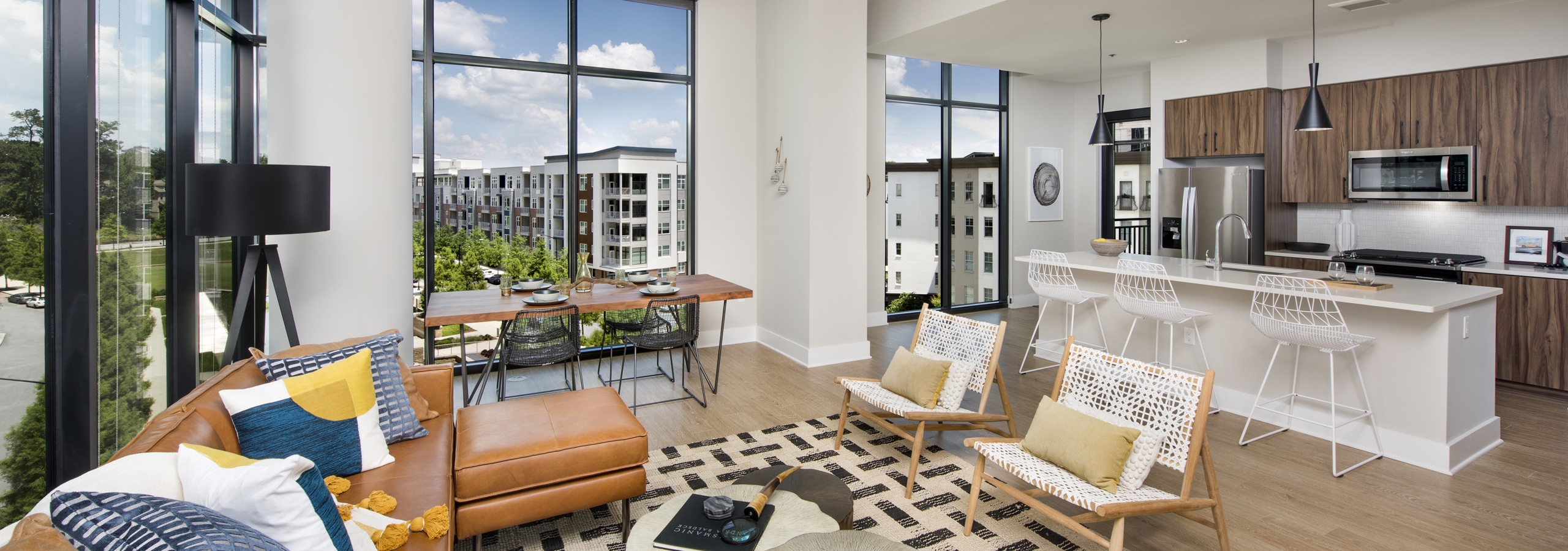 AMLI Lenox apartment interior with large windows and brown sofa with colorful pillows and dining area and island kitchen