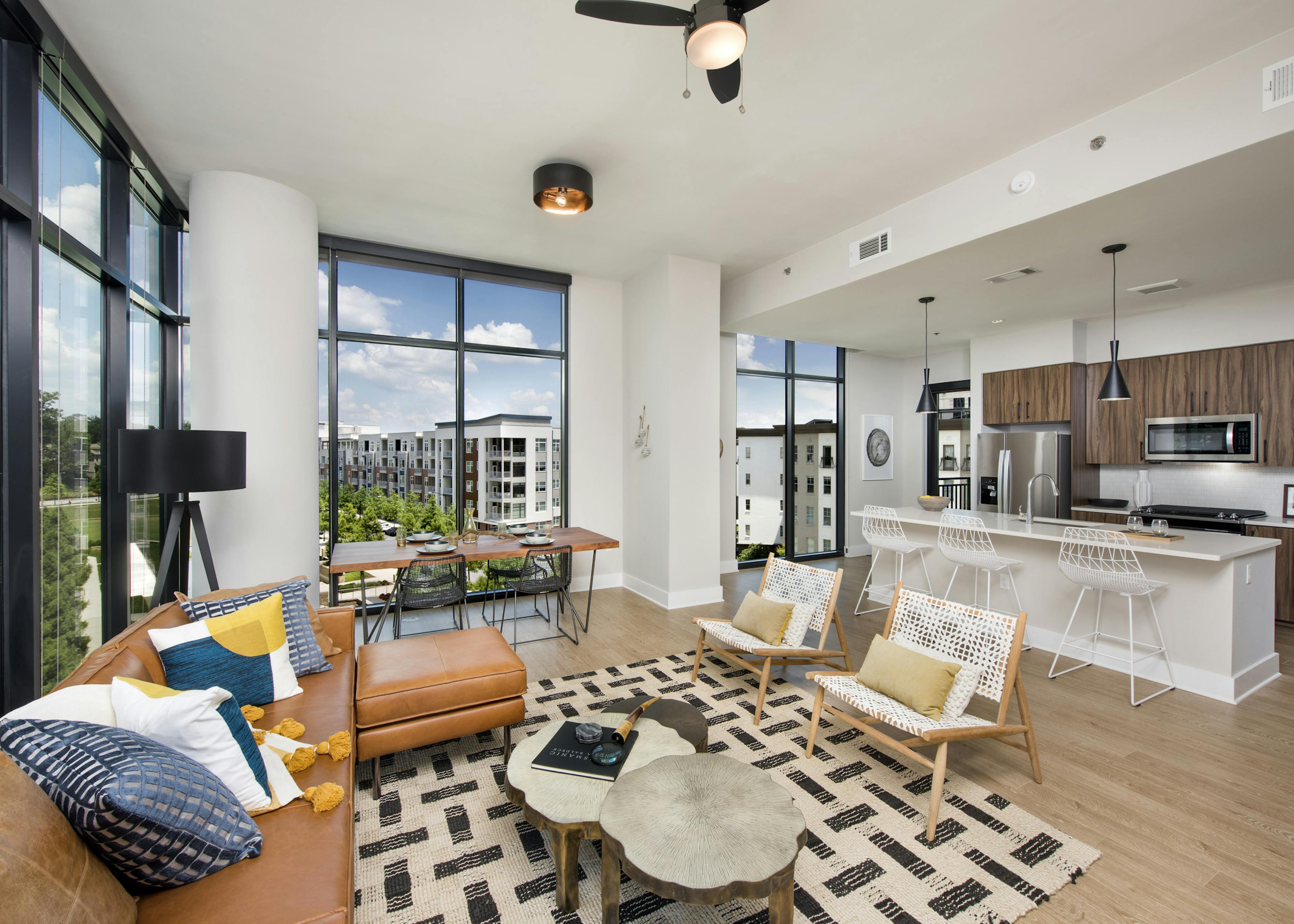 AMLI Lenox apartment interior with large windows and brown sofa with colorful pillows and dining area and island kitchen