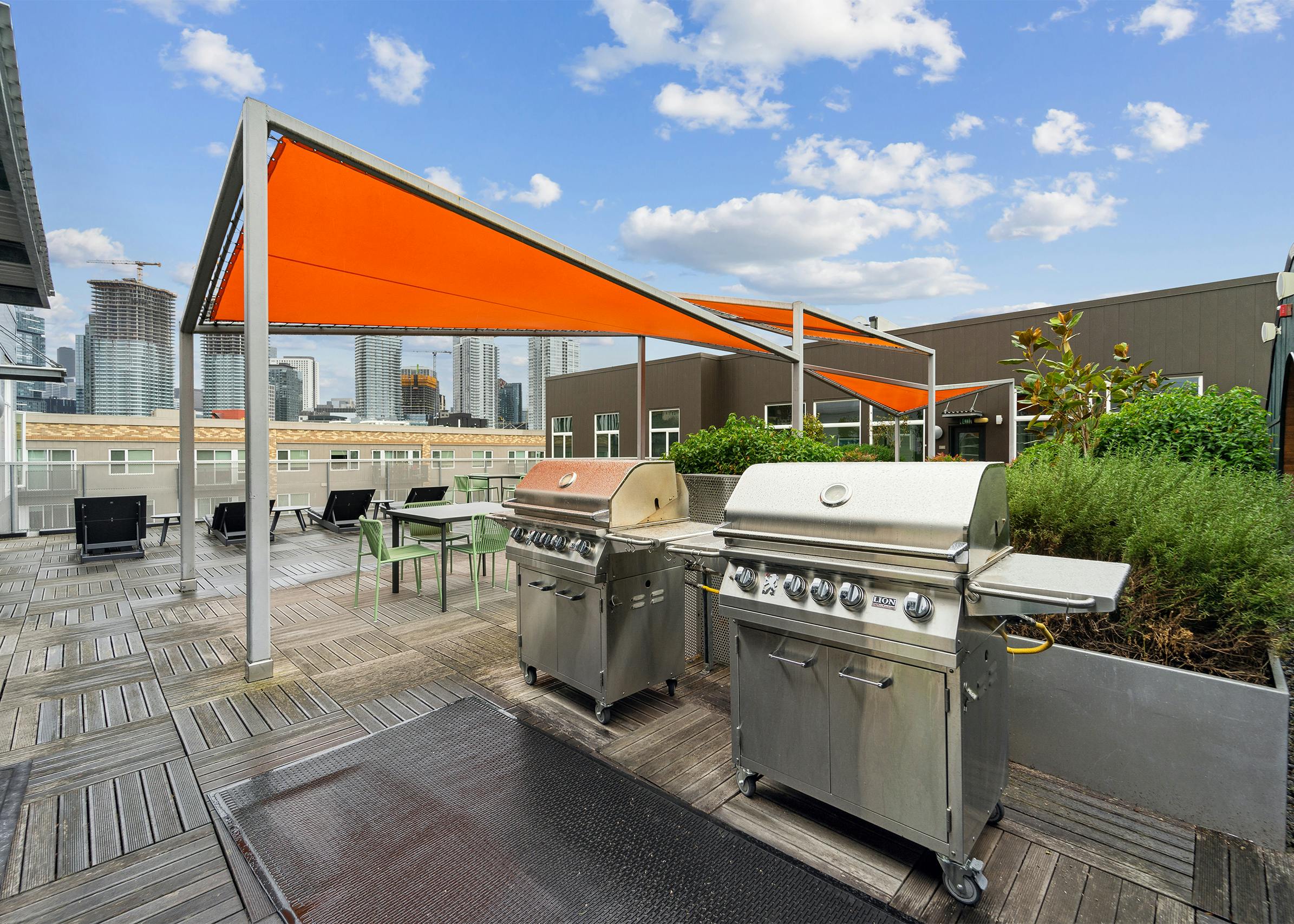 Rooftop deck at AMLI South Lake Union with two stainless steel grills as well as tables and chairs with orange canopies