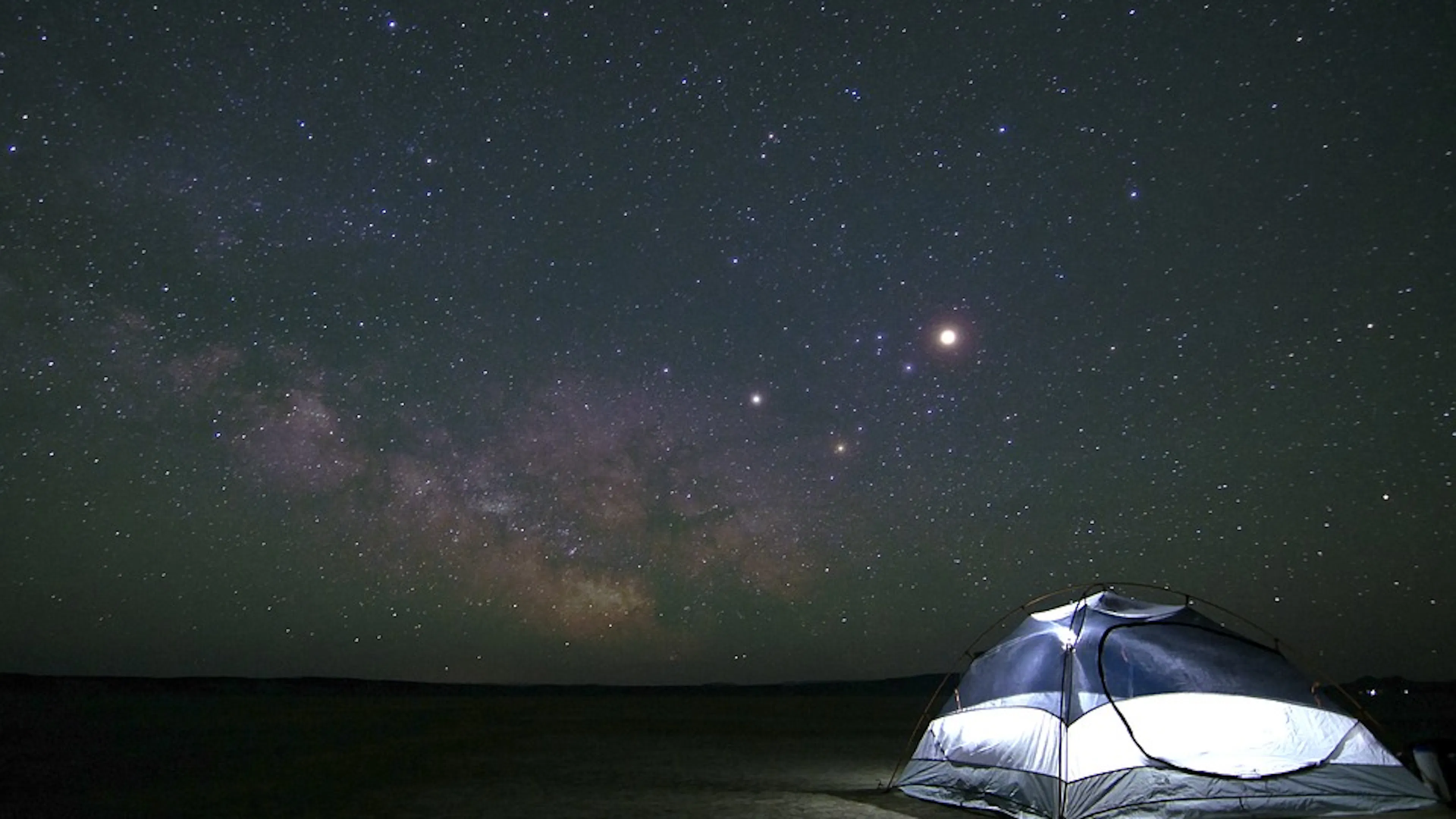 A camping tent in a field with a sky full of stars and the milky way shining through