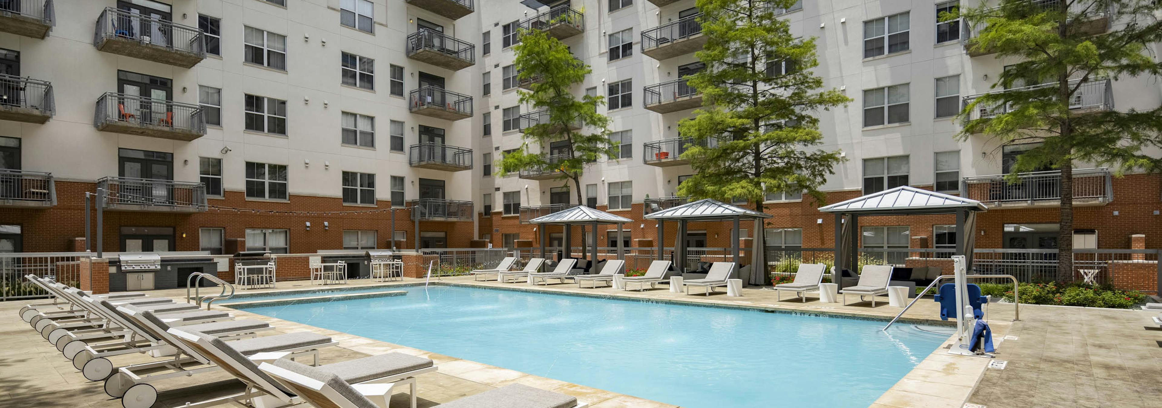 Daytime view of AMLI Downtown apartments courtyard pool with gray lounge seating and shaded cabanas with lounge seating