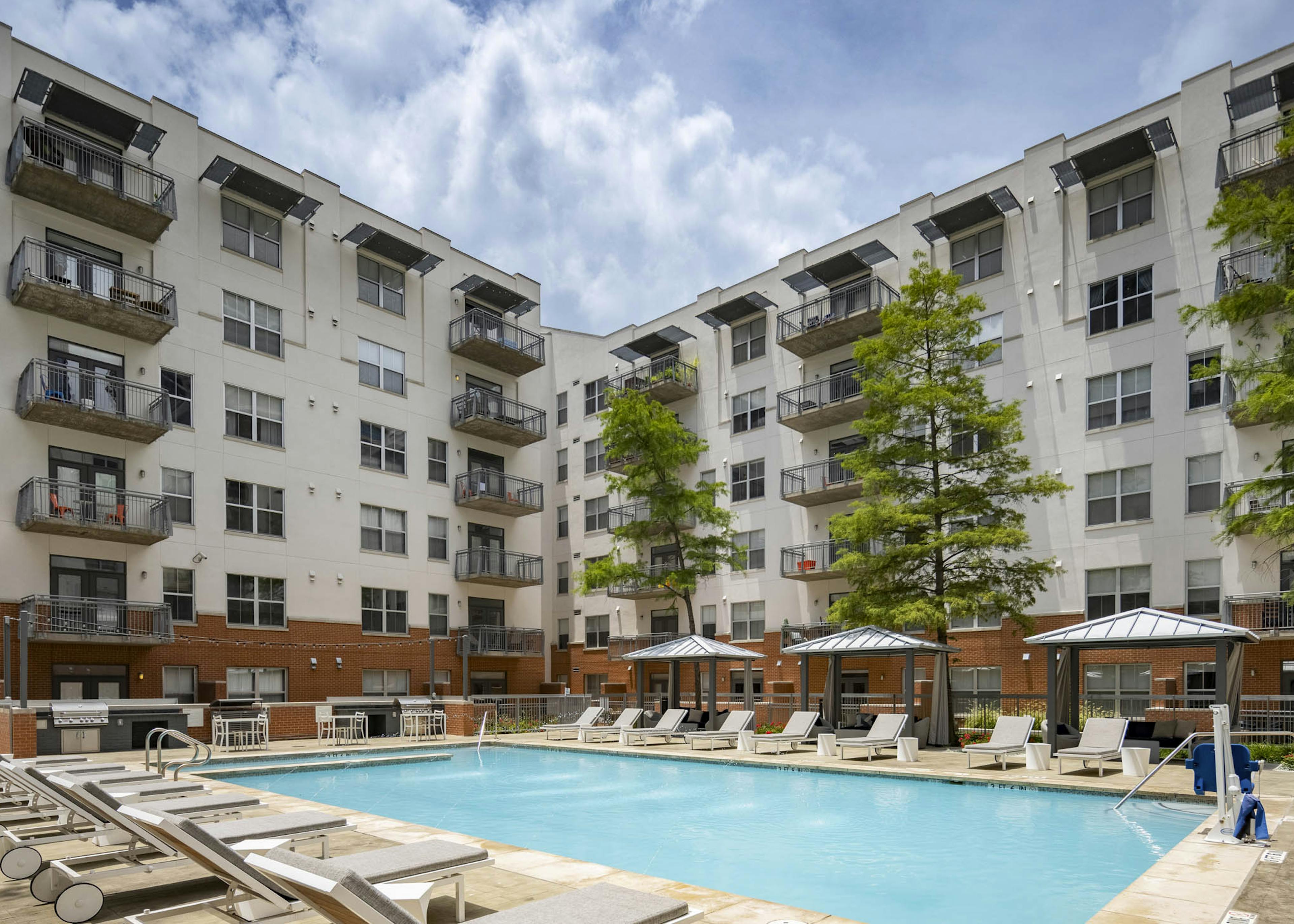 Daytime view of AMLI Downtown apartments courtyard pool with gray lounge seating and shaded cabanas with lounge seating