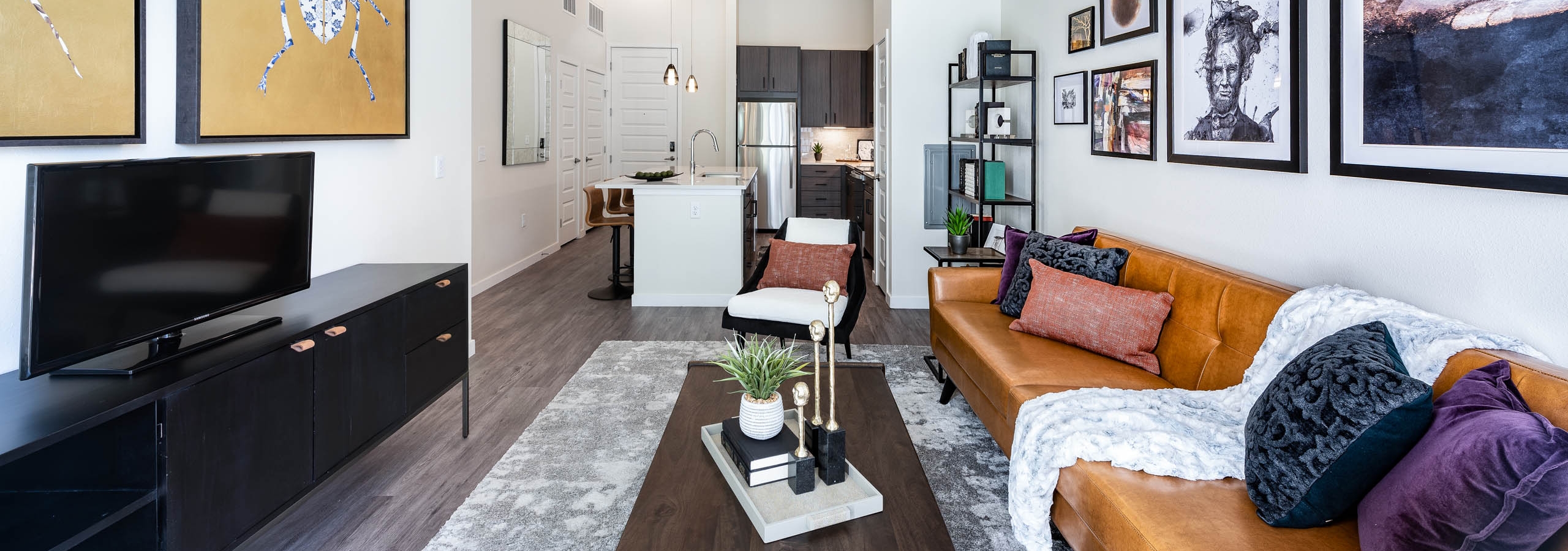 Apartment living room at AMLI Art District with a TV and leather couch and coffee table as well as a bookshelf and artwork