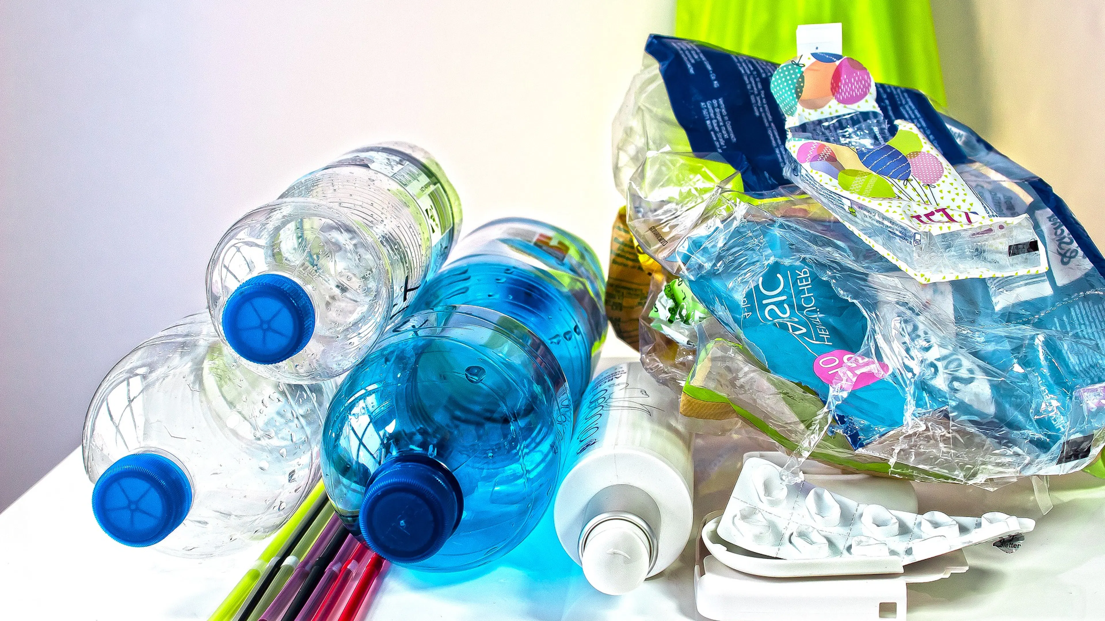 Three empty plastic bottles on a table next to a pile of crushed water bottles.