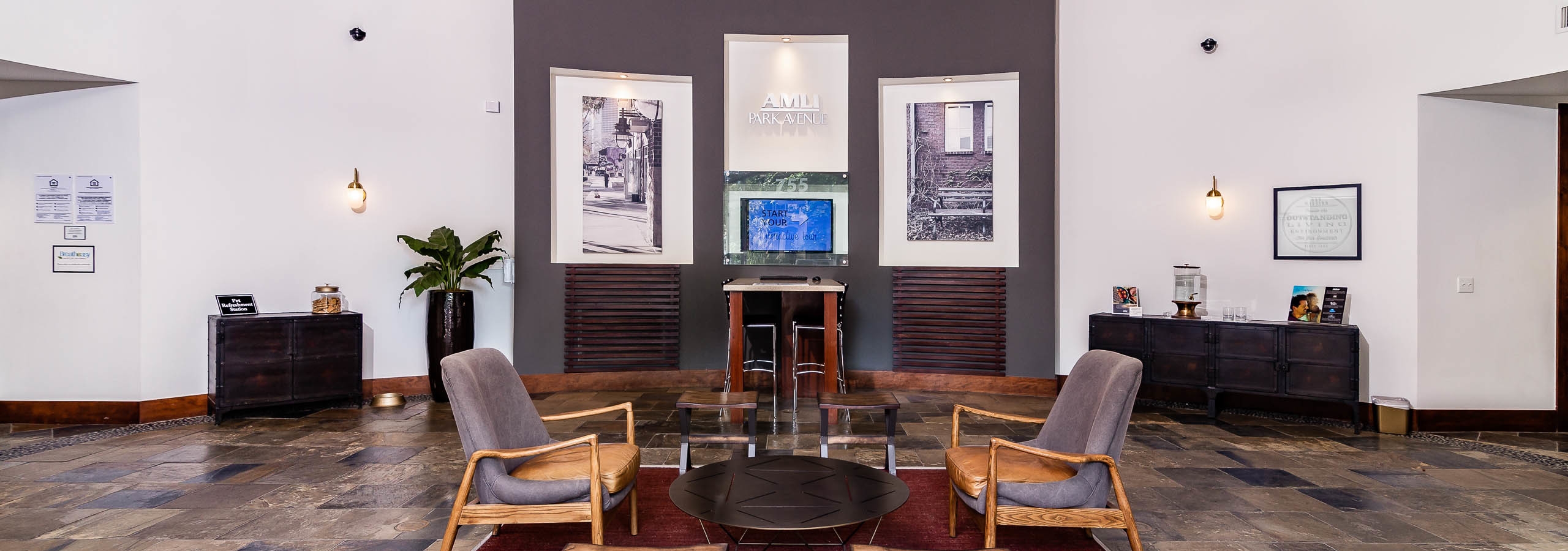 Lobby area at AMLI Park Ave apartments with chairs and a table and a desk with a computer and large pieces of wall artwork