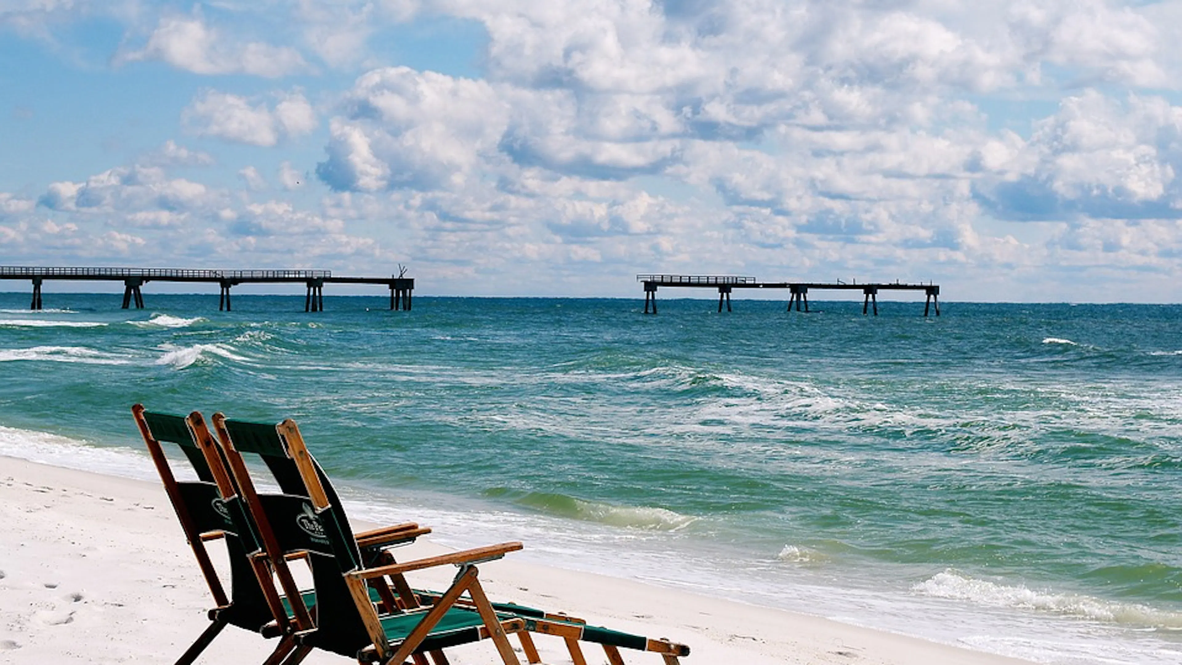 Two wooden beach chairs on a bright white sandy beach on a clear day