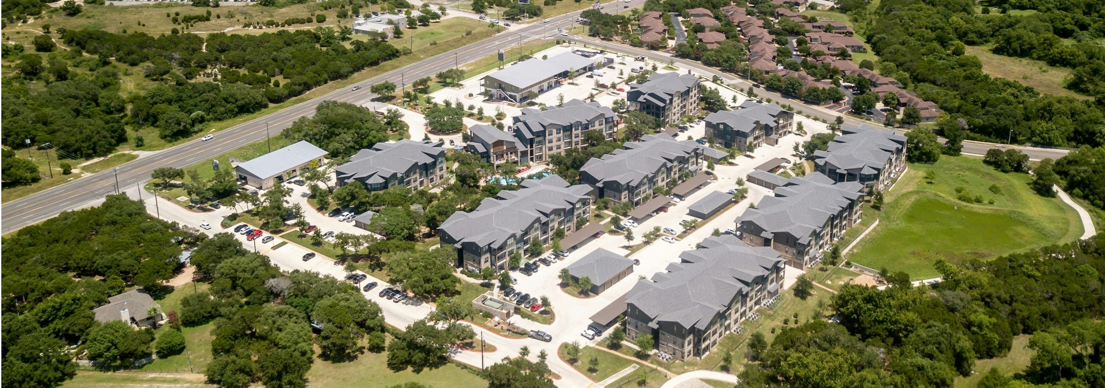 Daytime aerial view of AMLI Covered Bridge apartment community complex, retail buildings and parking areas