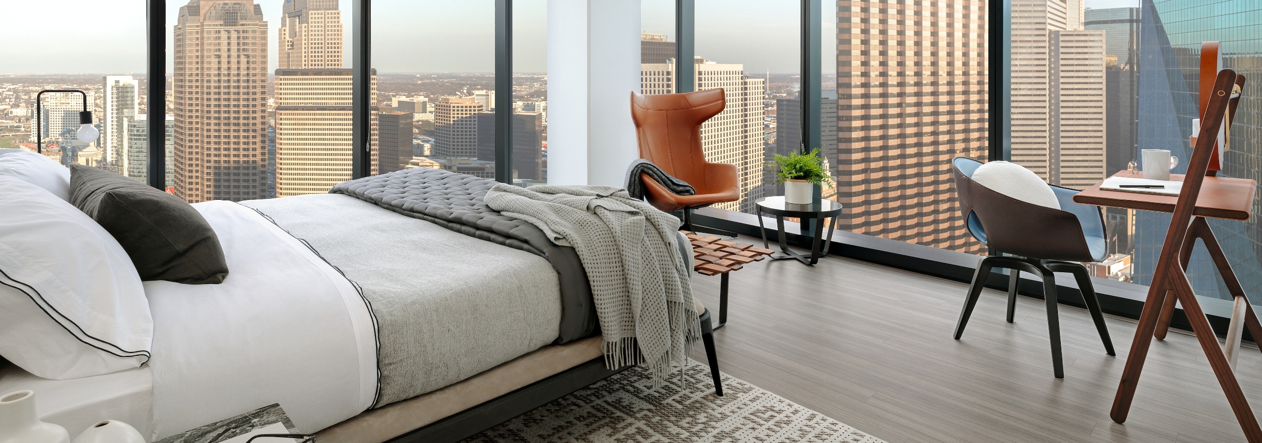 Interior of AMLI Fountain Place bedroom with white bedding and light wood floors and two walls of floor to ceiling windows