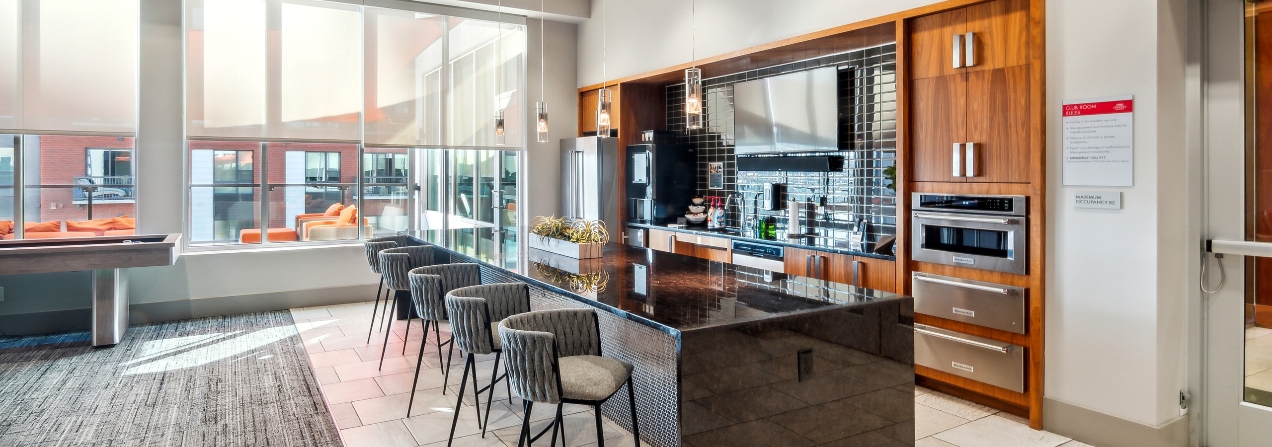 Resident kitchen at AMLI Denargo Market apartments with a long black island with chairs and a black tile back splash with TV
