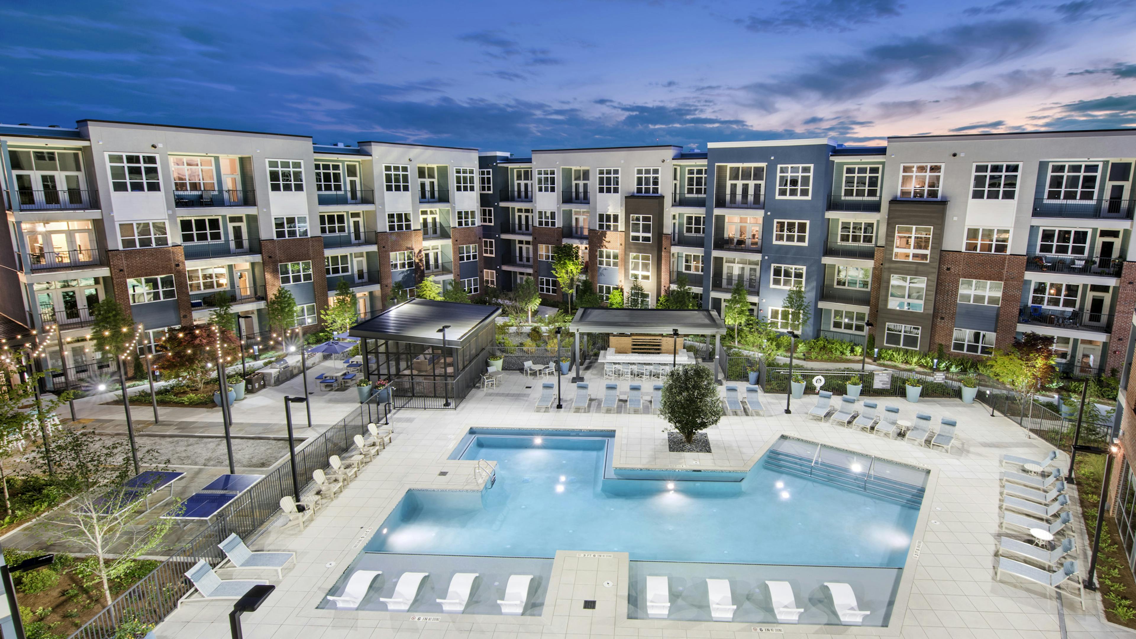 Overhead evening view of AMLI Decatur landscaped pool area with hanging lights and lounge chairs and uplit colorful building