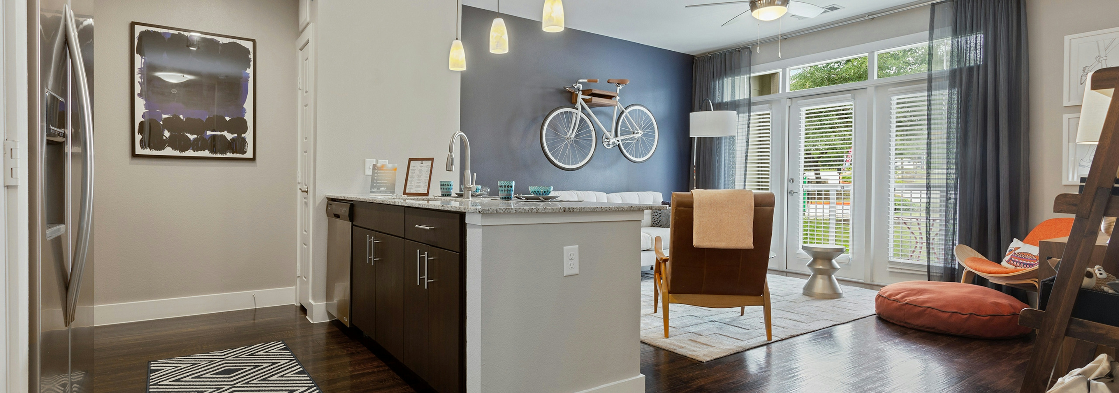 AMLI Covered Bridge living area during the day with large windows, plank flooring and espresso kitchen cabinets