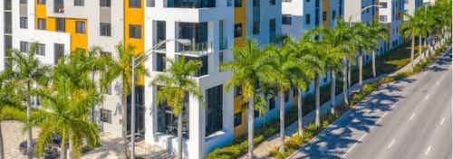 Building exterior view of AMLI 8800 painted with vibrant yellow and white colors surrounded by a palm tree lined street