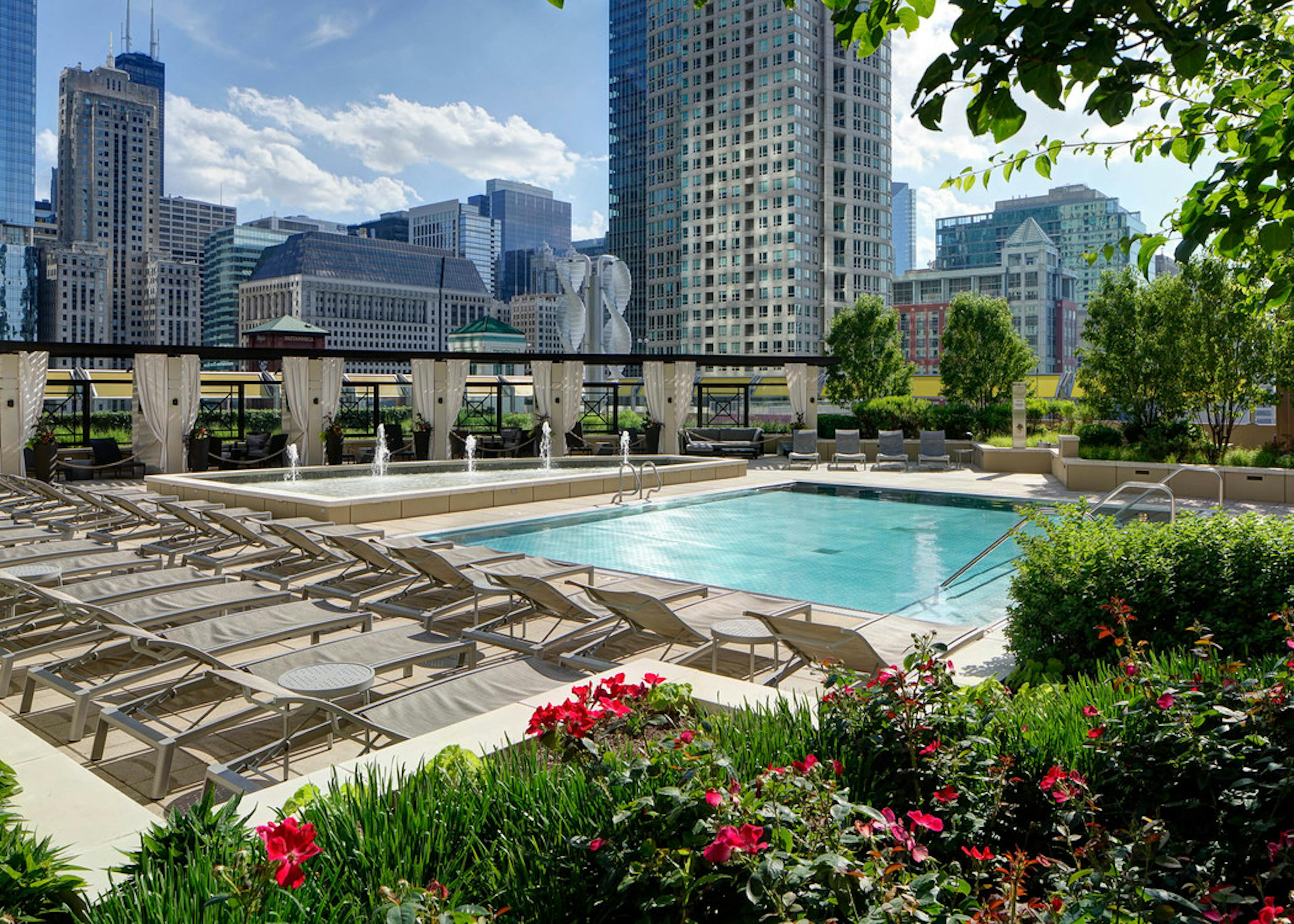 Rooftop pool deck at AMLI River North surrounded by lush landscaping and pool chairs and private cabanas with city skyline
