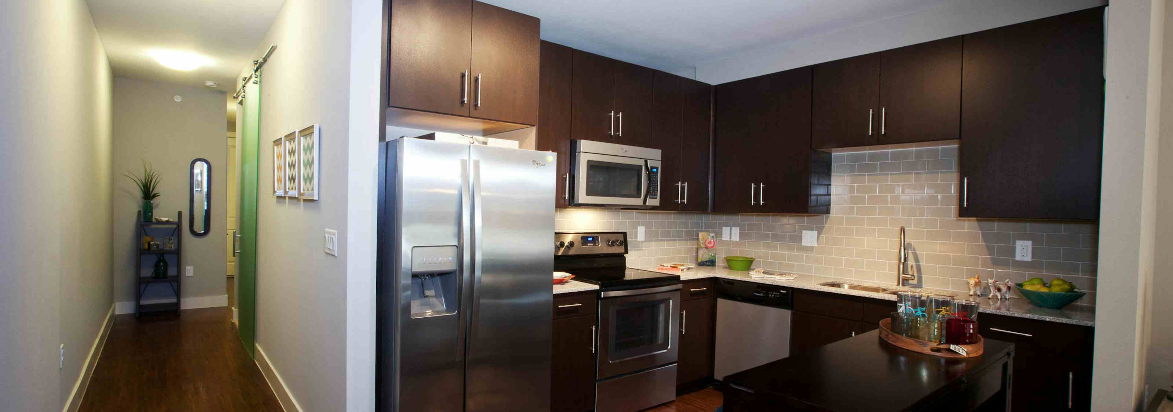 A kitchen at AMLI Riverfront Park apartments with stainless steel appliances and cupboards and a view of the front door