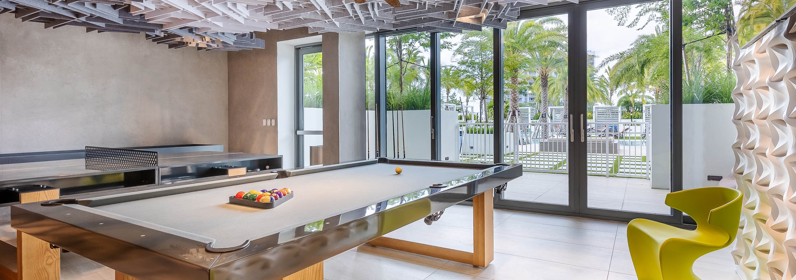The Arcade at AMLI Midtown Miami apartments with a pool and ping pong table and a geometric ceiling and alligator chandelier