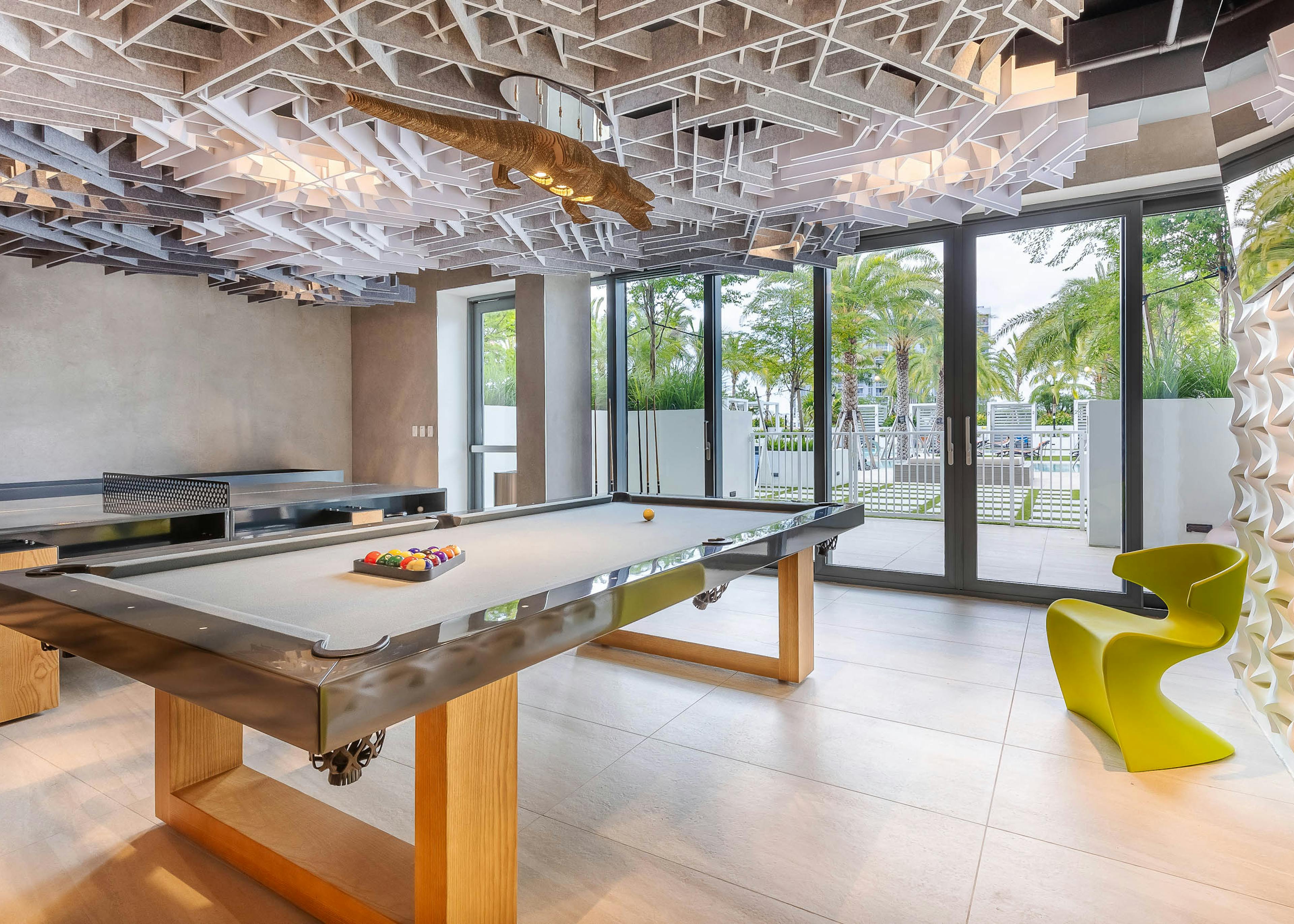 The Arcade at AMLI Midtown Miami apartments with a pool and ping pong table and a geometric ceiling and alligator chandelier 