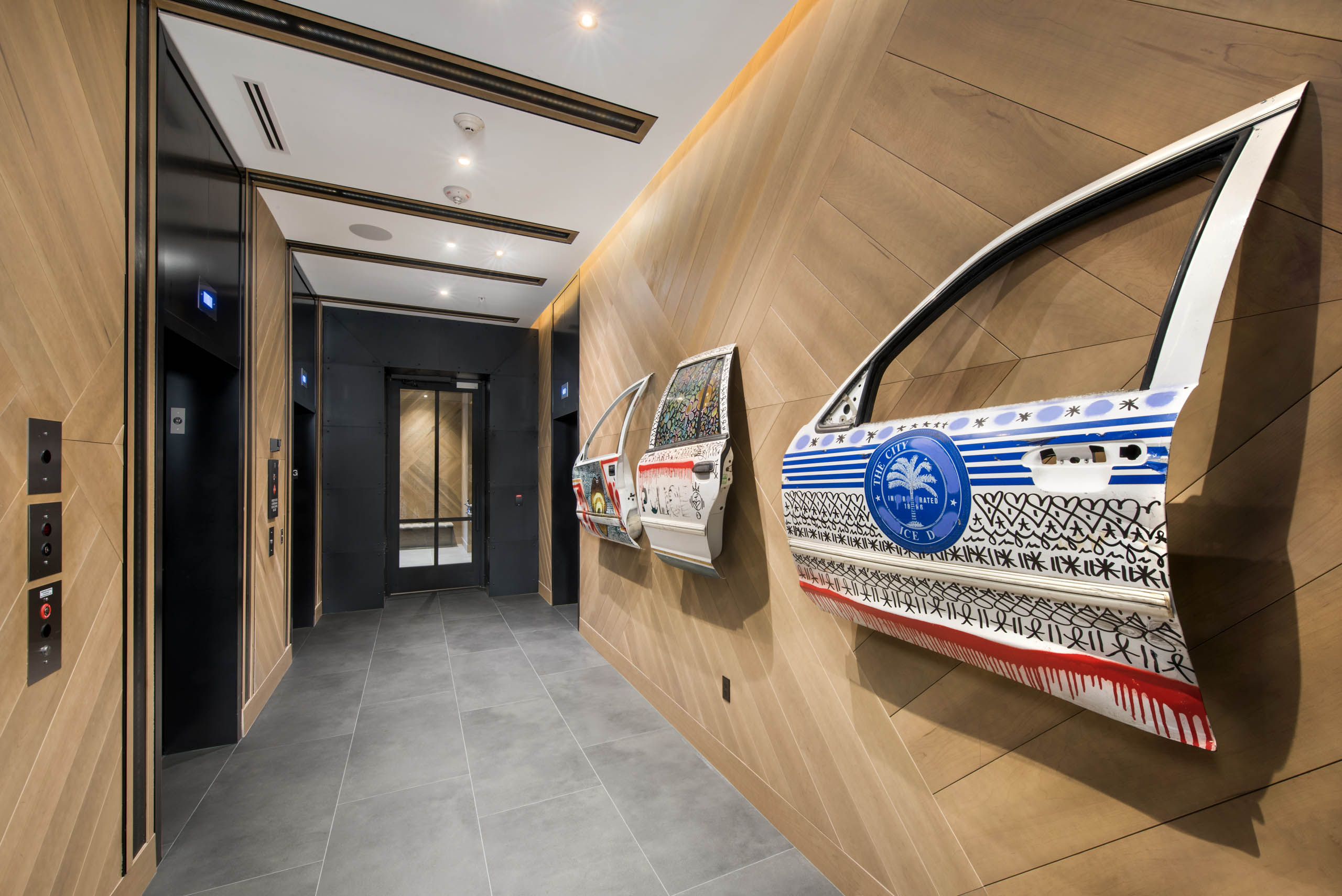 Lobby hall with detailed artwork painted on car doors hung on wood slat wall near elevator bank at AMLI Midtown 29