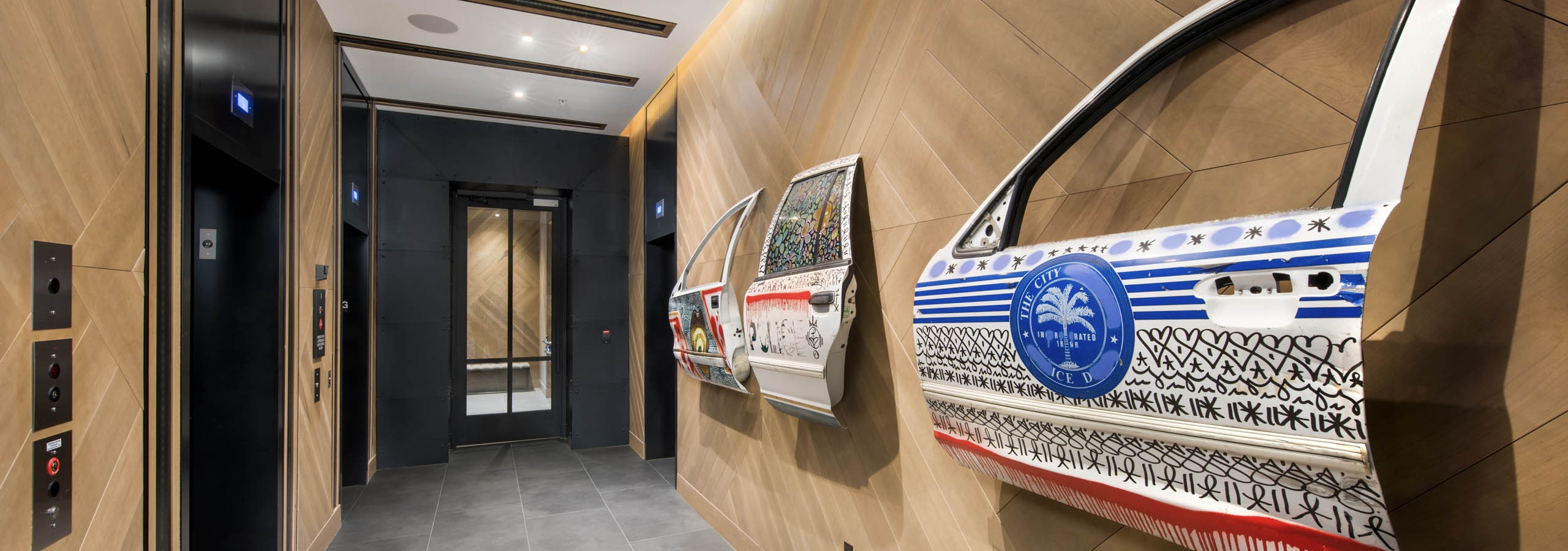 Lobby hall with detailed artwork painted on car doors hung on wood slat wall near elevator bank at AMLI Midtown 29