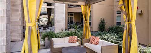 Daytime view of curtained cabana with outdoor lounge sofas and decorative orange accent pillows at AMLI RidgeGate apartments