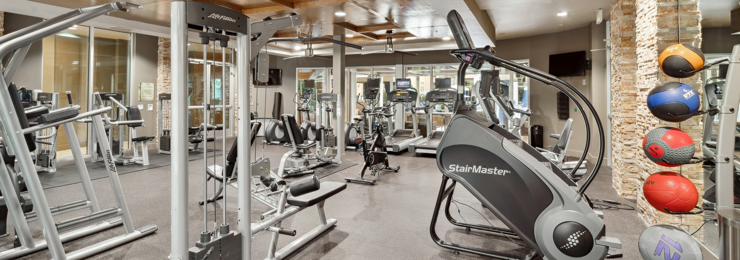 Interior view of a fitness center at AMLI RidgeGate with strength training equipment and cardio equipment and medicine balls
