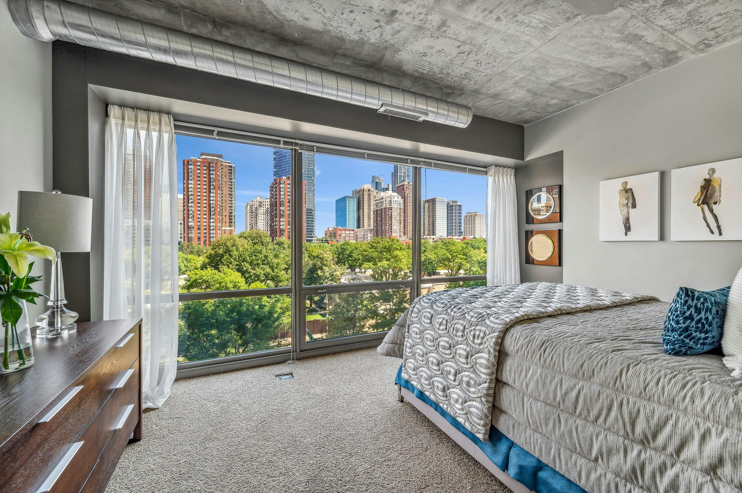 AMLI 900 bedroom with floor to ceiling view of city and bed with gray comforter and carpet and artwork on gray wall
