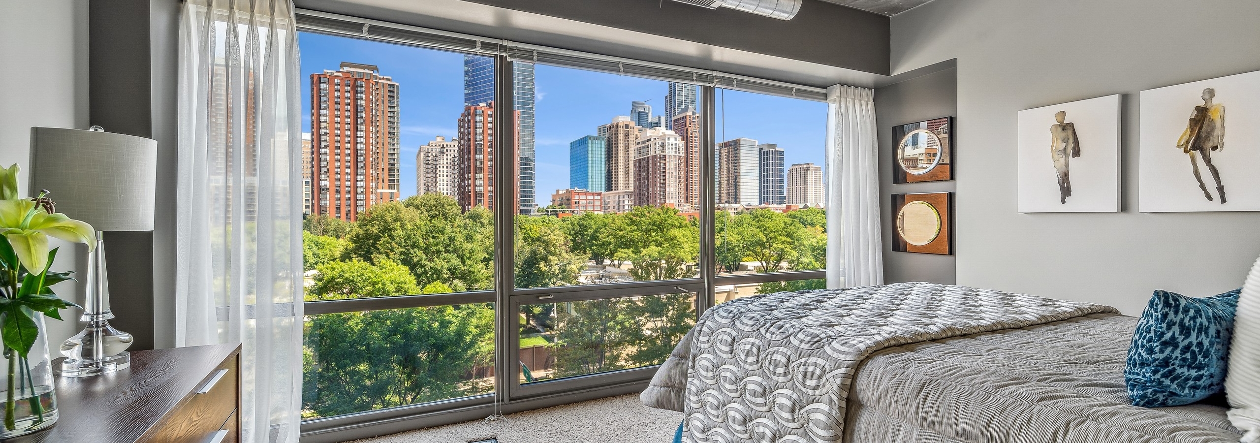 AMLI 900 bedroom with floor to ceiling view of city  and bed with gray comforter and carpet and artwork on gray wall
