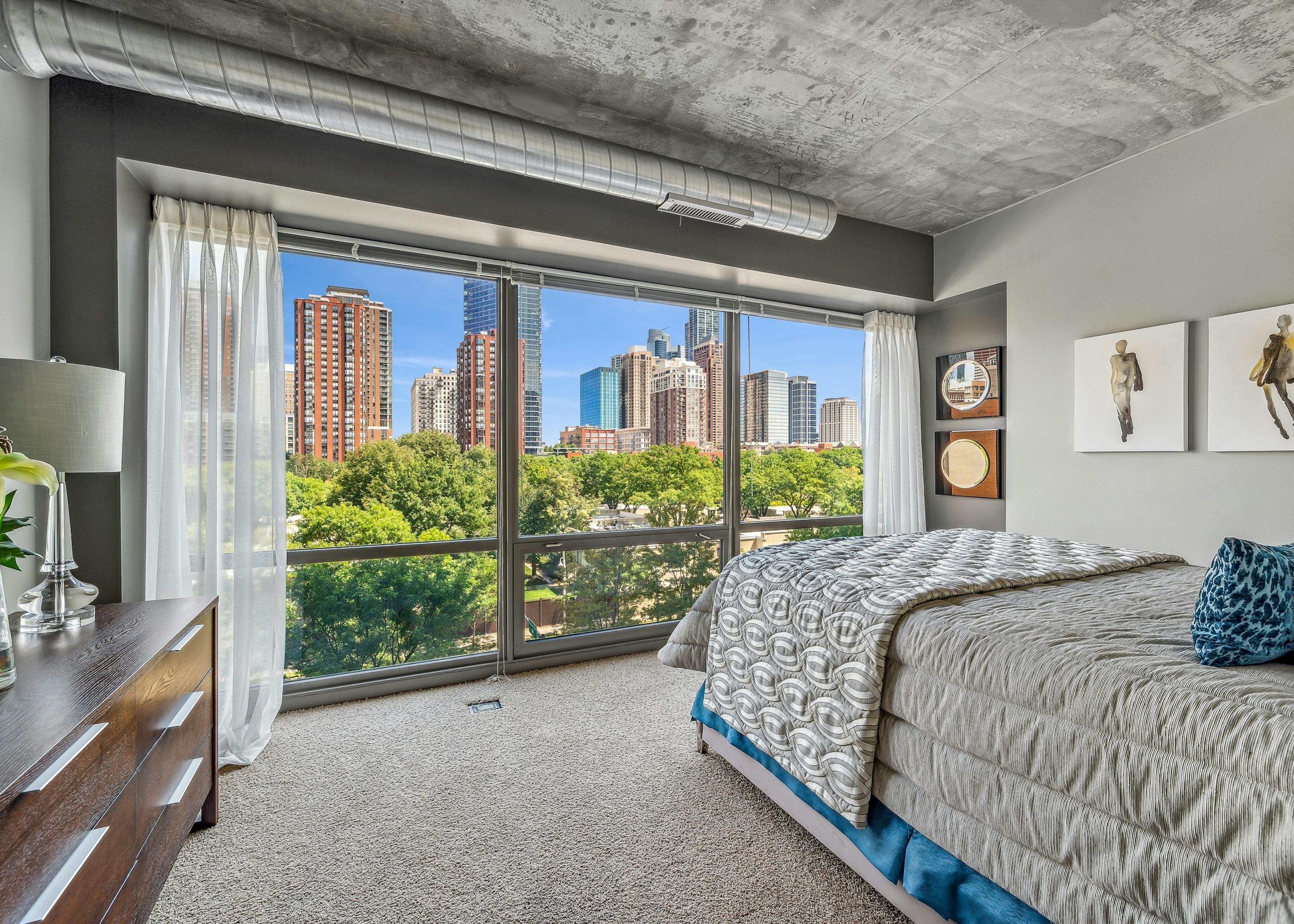 AMLI 900 bedroom with floor to ceiling view of city  and bed with gray comforter and carpet and artwork on gray wall