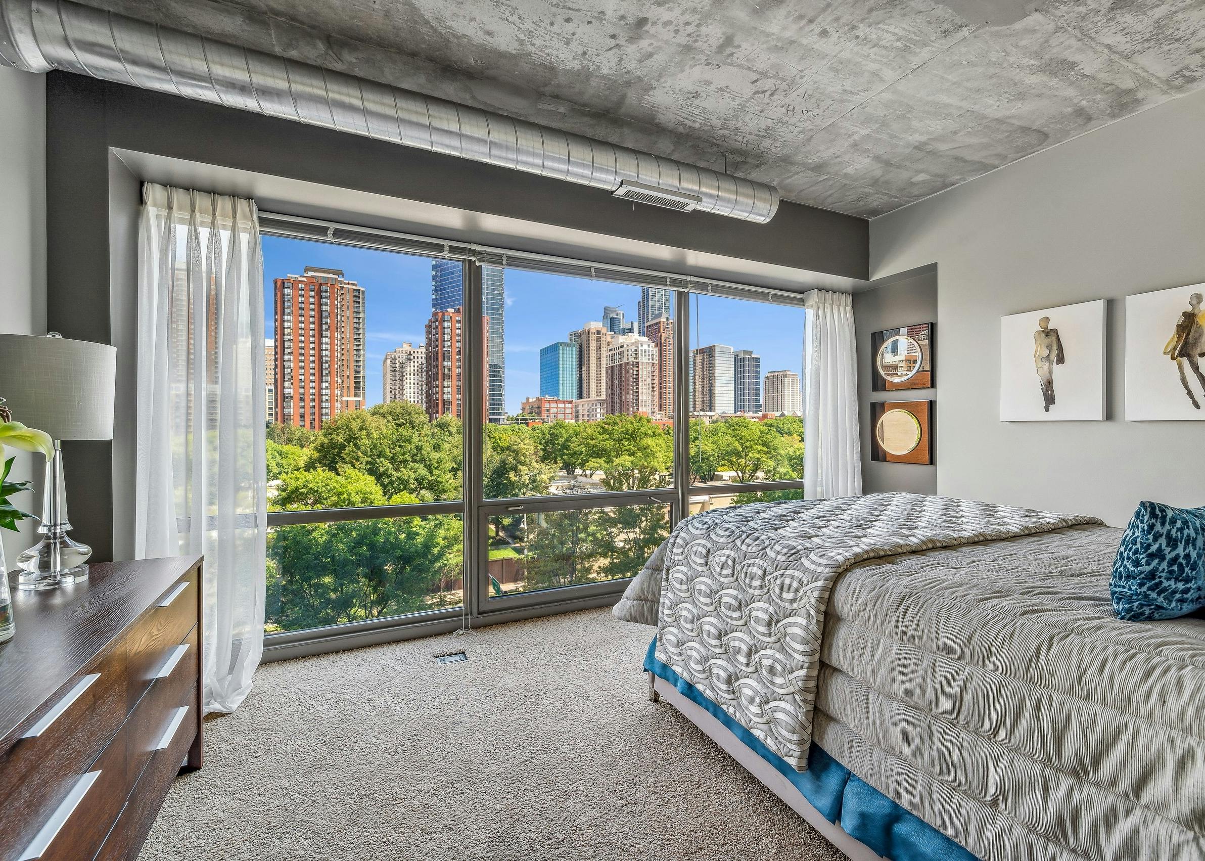 AMLI 900 bedroom with floor to ceiling view of city and bed with gray comforter and carpet and artwork on gray wall