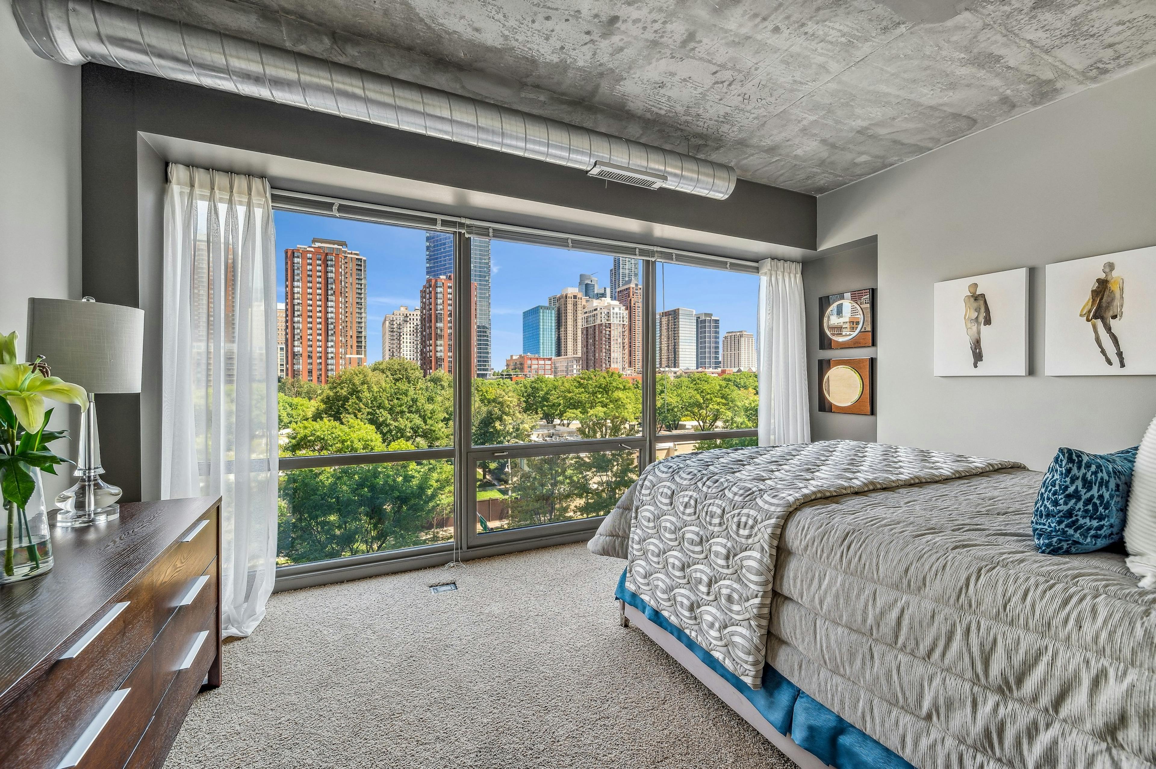 AMLI 900 bedroom with floor to ceiling view of city  and bed with gray comforter and carpet and artwork on gray wall