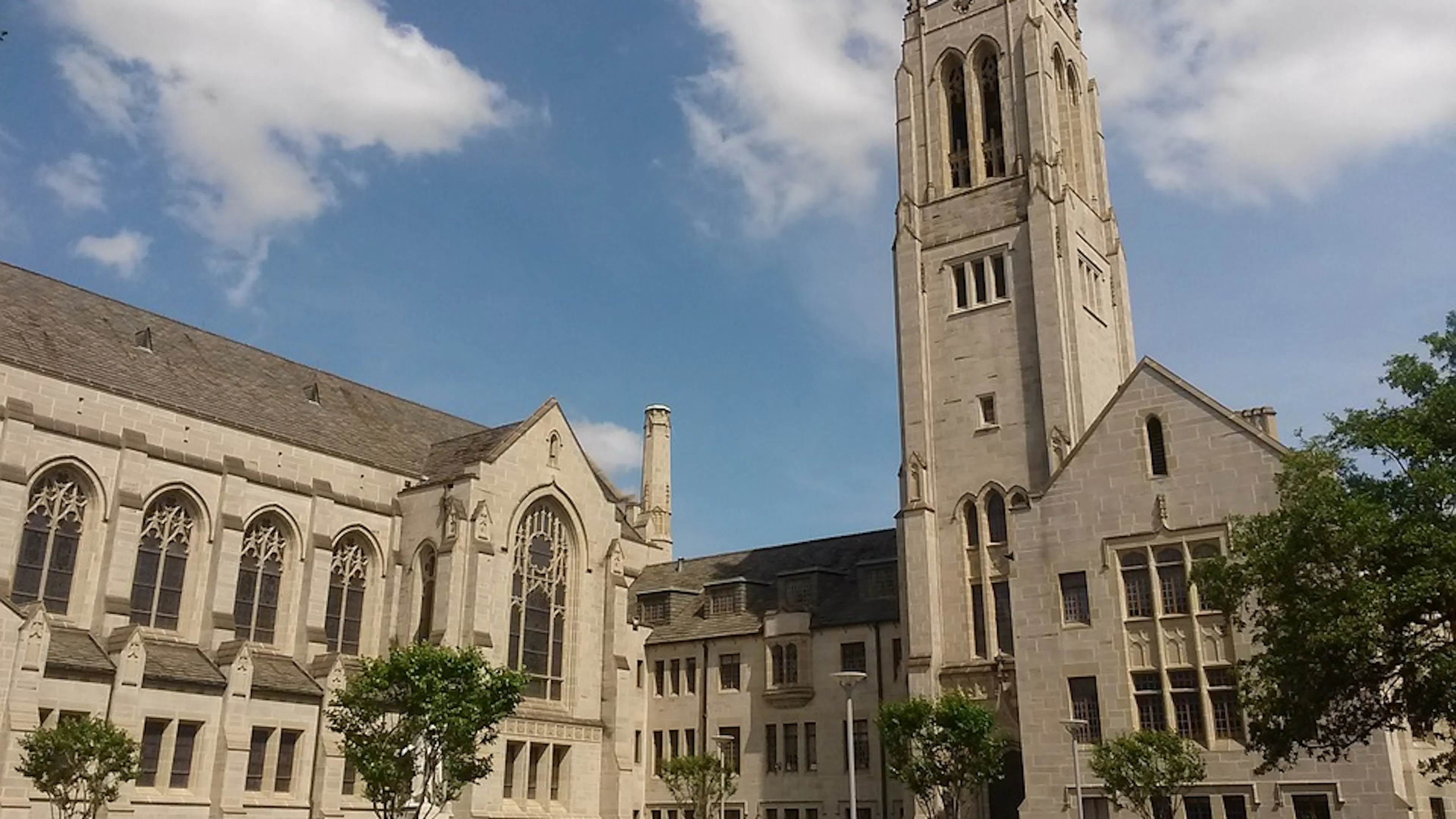 A large stone church with some trees and bushes around it set against a blue sky