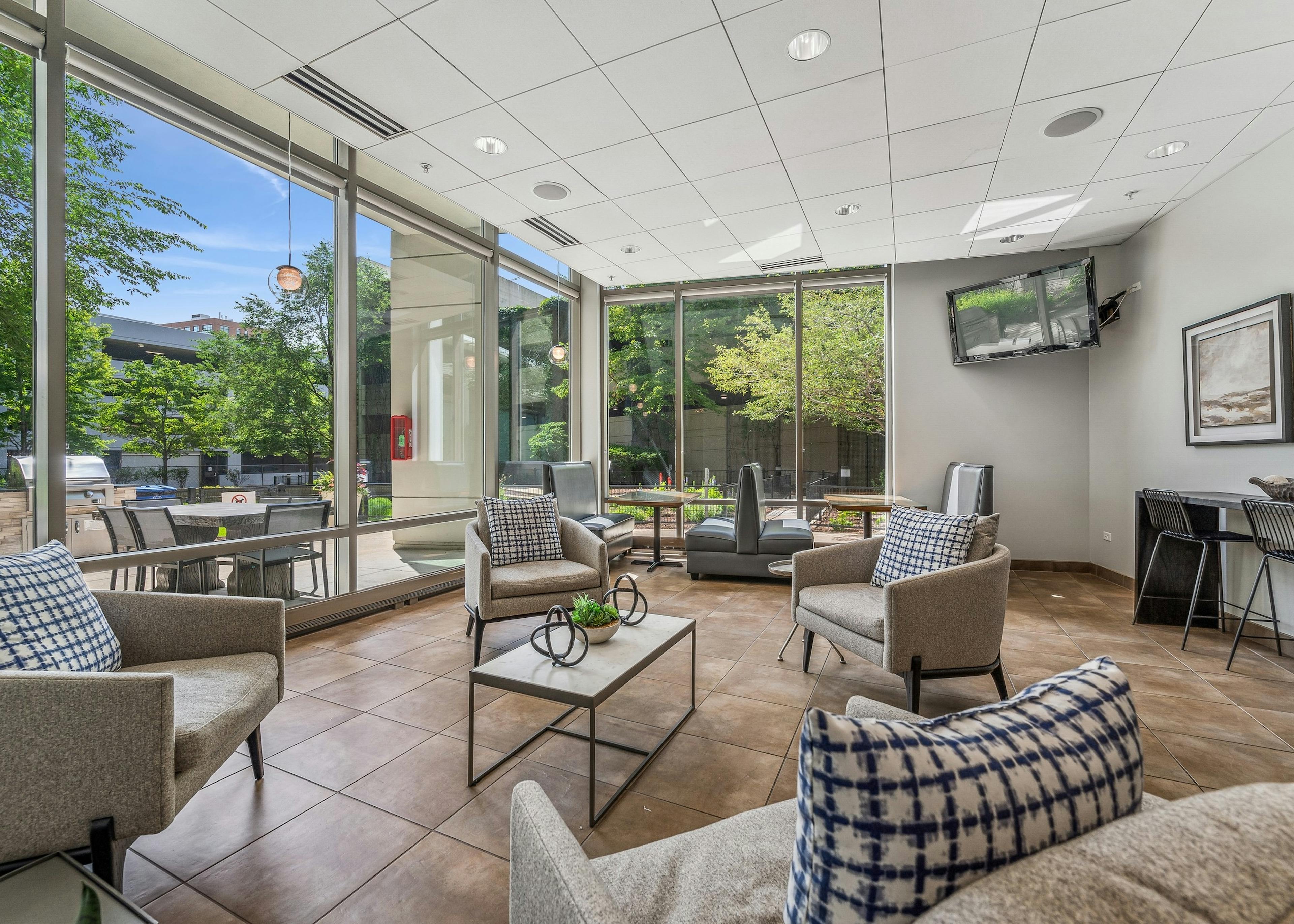 AMLI 900 lounge with tan chairs and blue and white pillows and brown tile floor with wall TV and view to the exterior