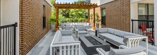 AMLI Quadrangle shaded courtyard fire pit area with gray cushion seating and a wood pergola with lush greenery in the back