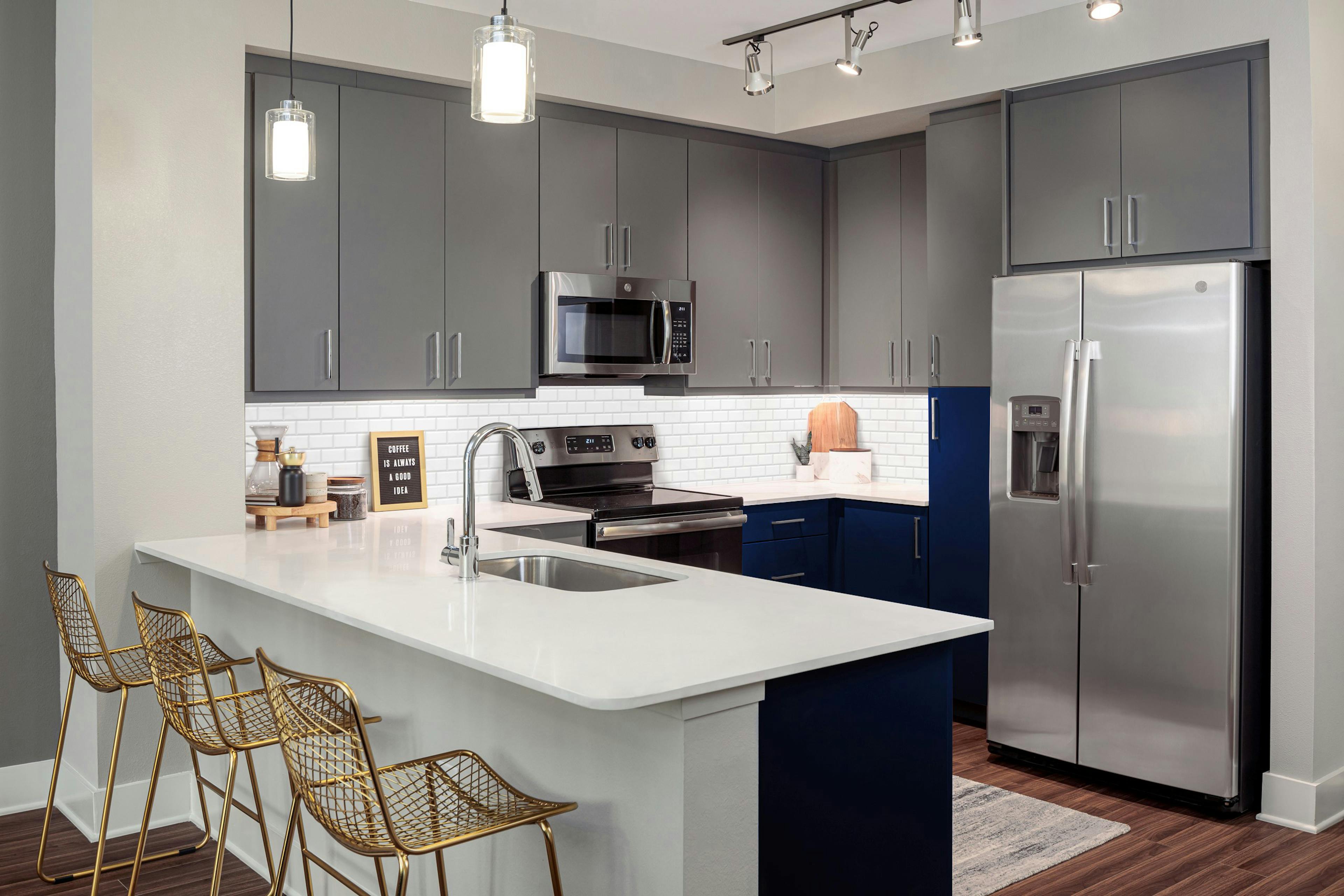 Kitchen at AMLI Branch Park apartments with gray cabinets and white countertops and stainless steel appliances