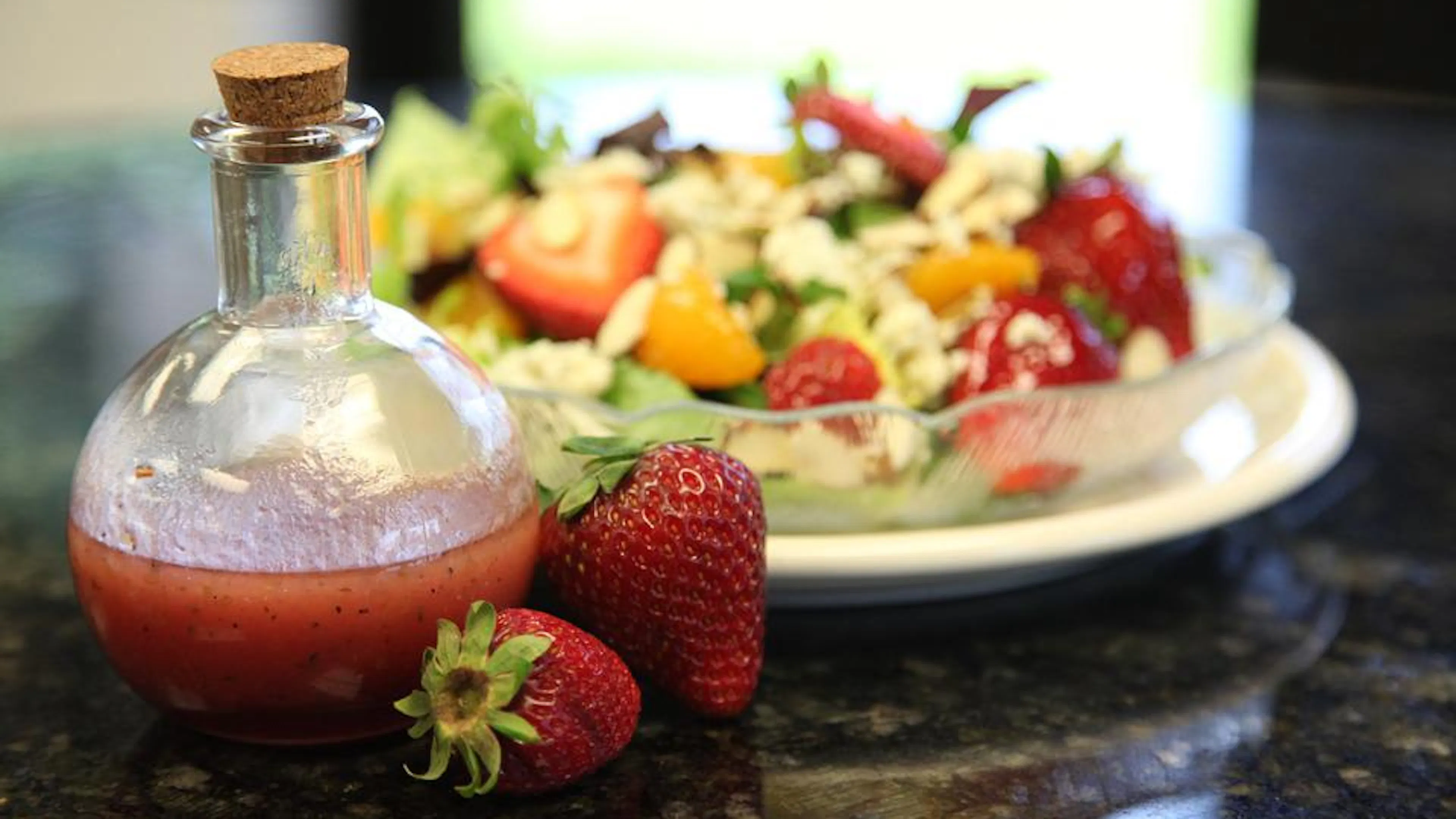 A rounded jar full of strawberry vinaigrette salad dressing next to a plate of garden salad