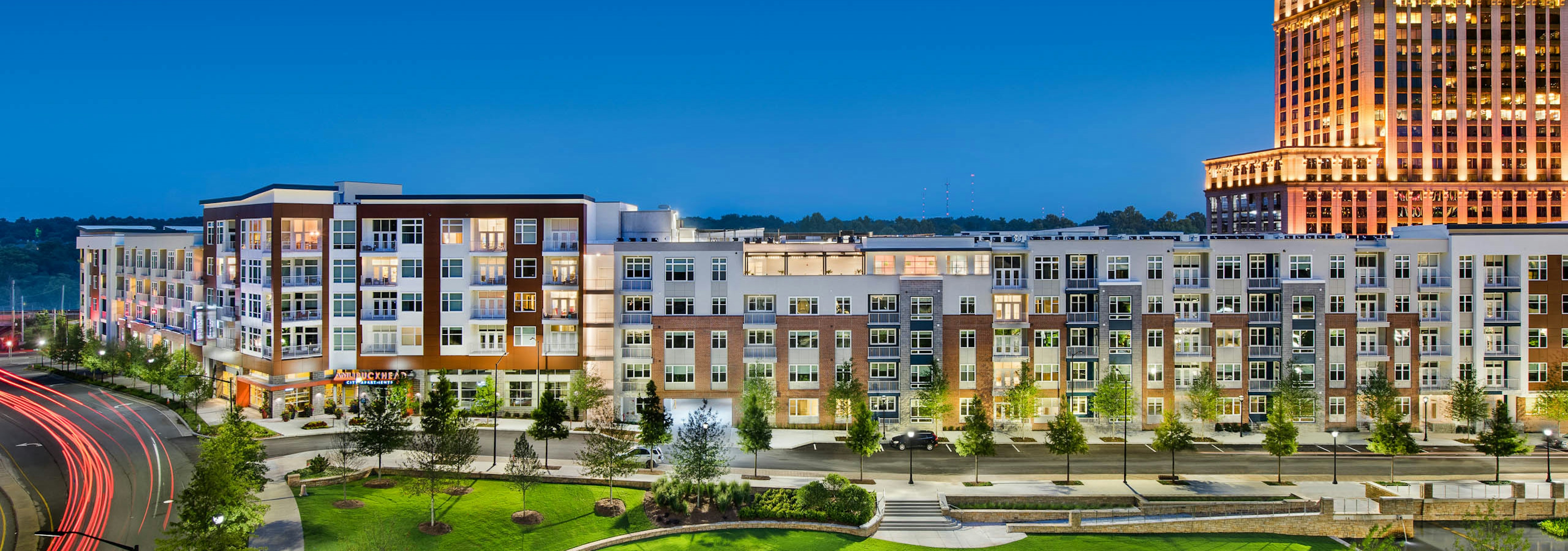 Exterior of AMLI Buckhead apartment community at night with light coming through the windows and trees lining the sidewalk