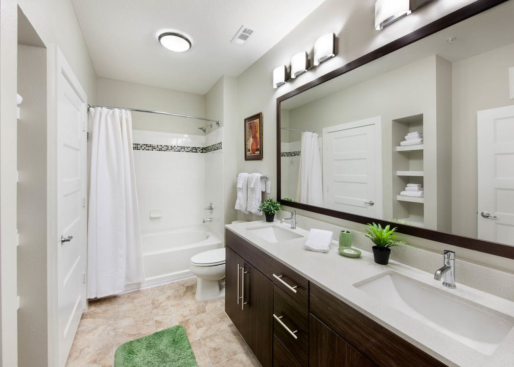 Interior of AMLI Piedmont Heights bathroom with a double dark wood vanity and mirror with a toilet and white shower tub