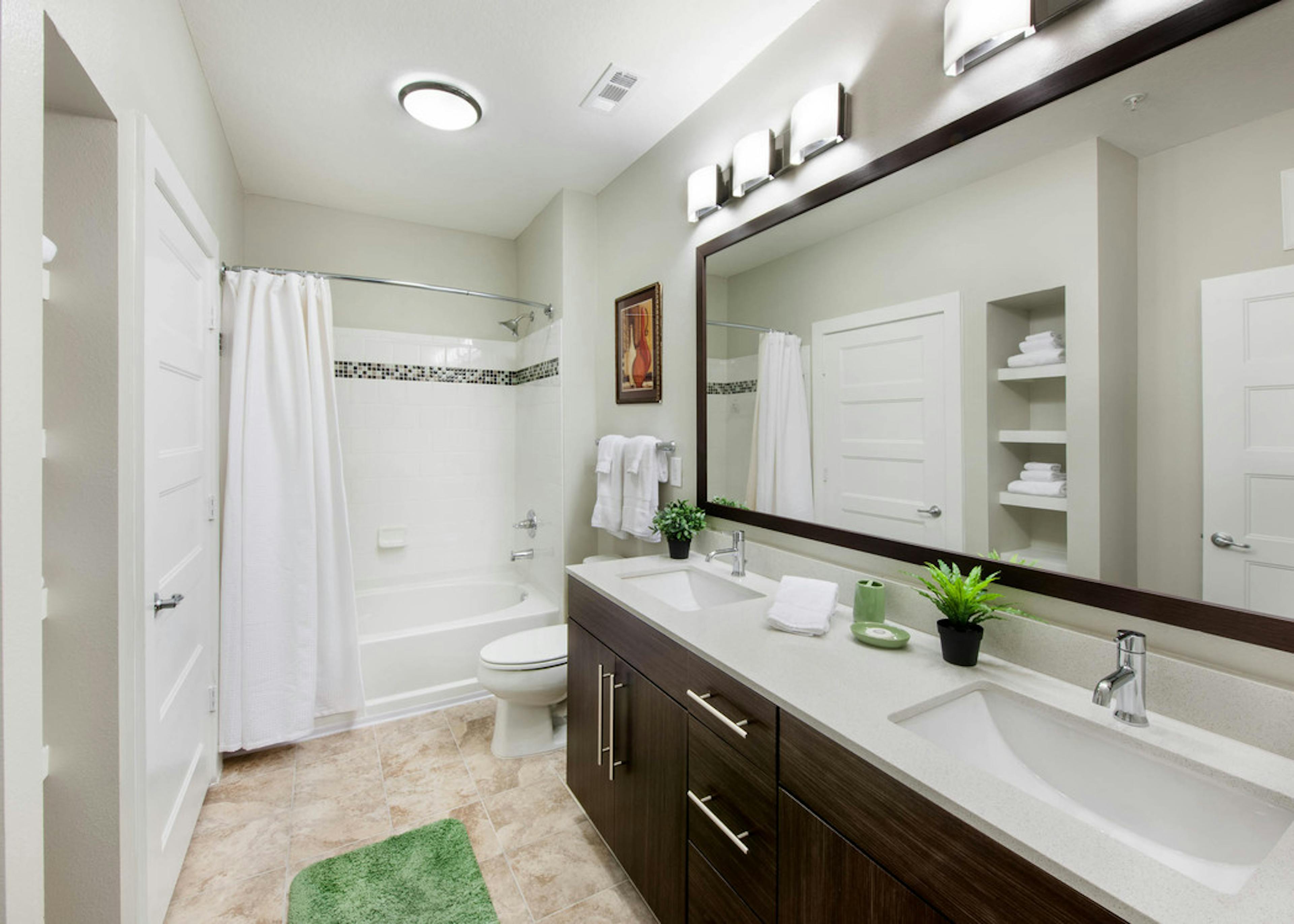 Interior of AMLI Piedmont Heights bathroom with a double dark wood vanity and mirror with a toilet and white shower tub 