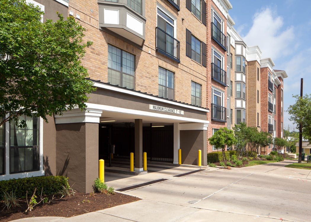 Exterior daytime view of AMLI Eastside parking garage entrance with bright trees and a blue sky in the background