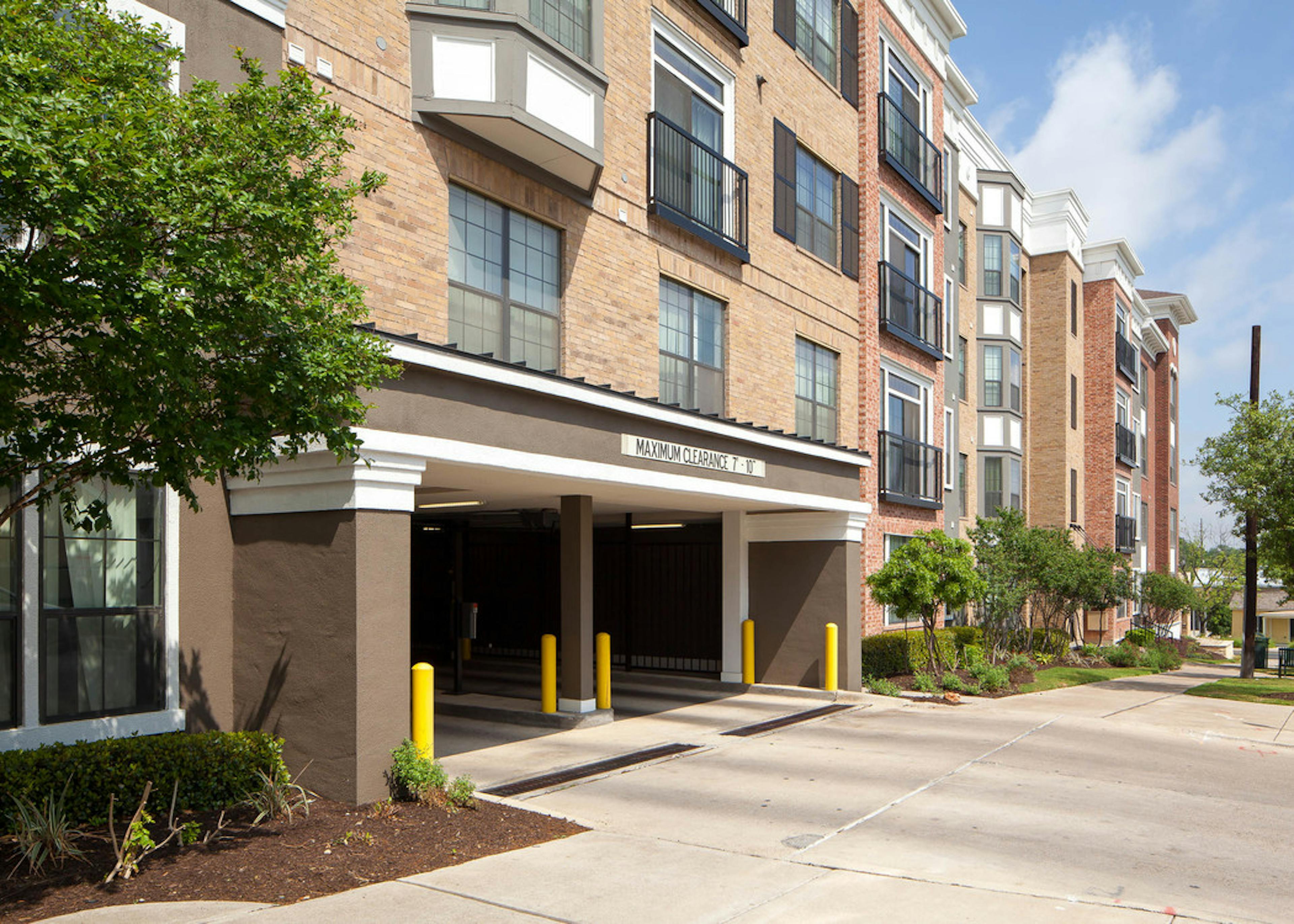 Exterior daytime view of AMLI Eastside parking garage entrance with bright trees and a blue sky in the background