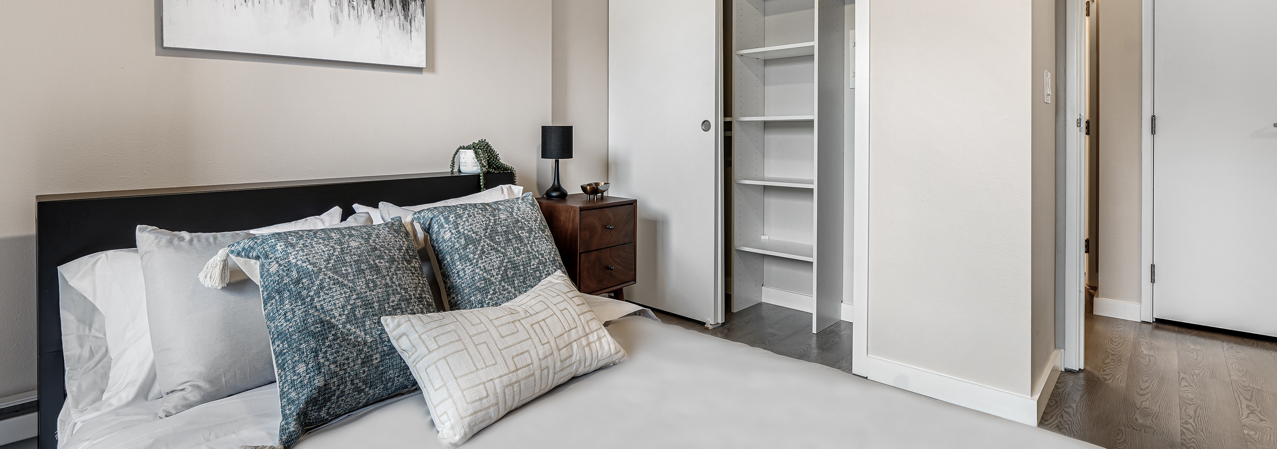 AMLI Bellevue Park bedroom with queen bed with light grey bedding and brown nightstand and white closet with built ins