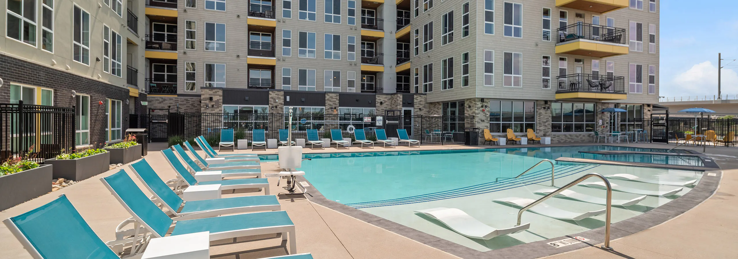 AMLI RiNo pool with lounge seating inside and outside of water and beige and brown building with yellow balconies