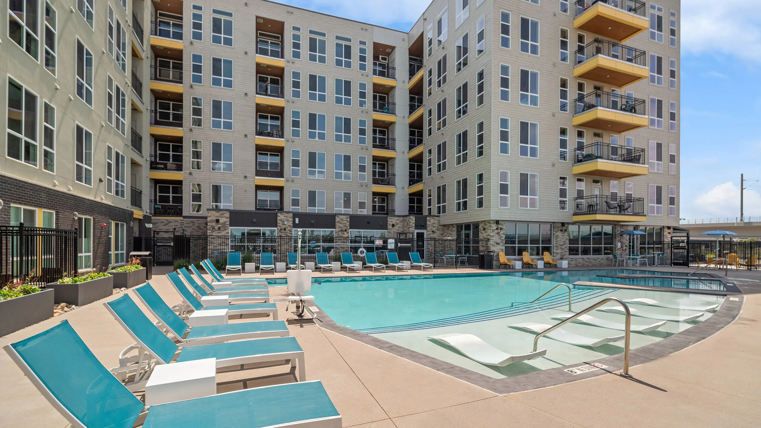 AMLI RiNo pool with lounge seating inside and outside of water and beige and brown building with yellow balconies