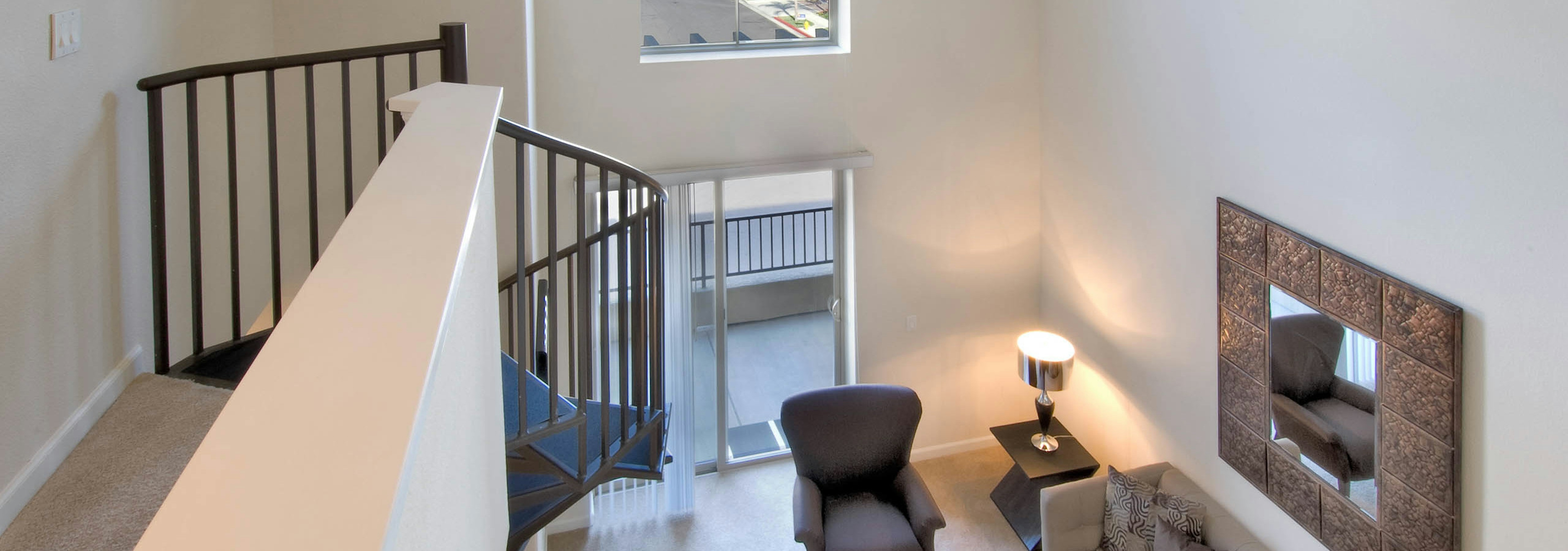 Interior view of AMLI Warner Center apartment loft’s upper level facing down to furnished living room area with framed mirror