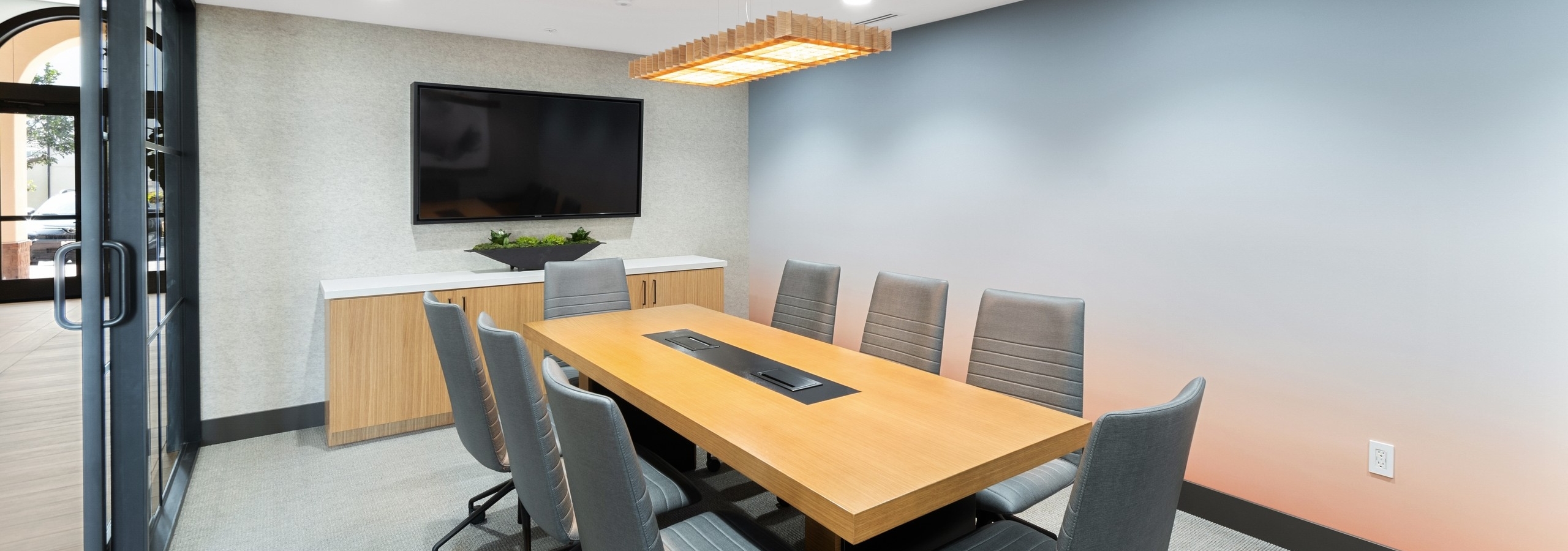 Conference room with large wooden table and gray chairs and big screen TV at AMLI Spanish Hills apartments