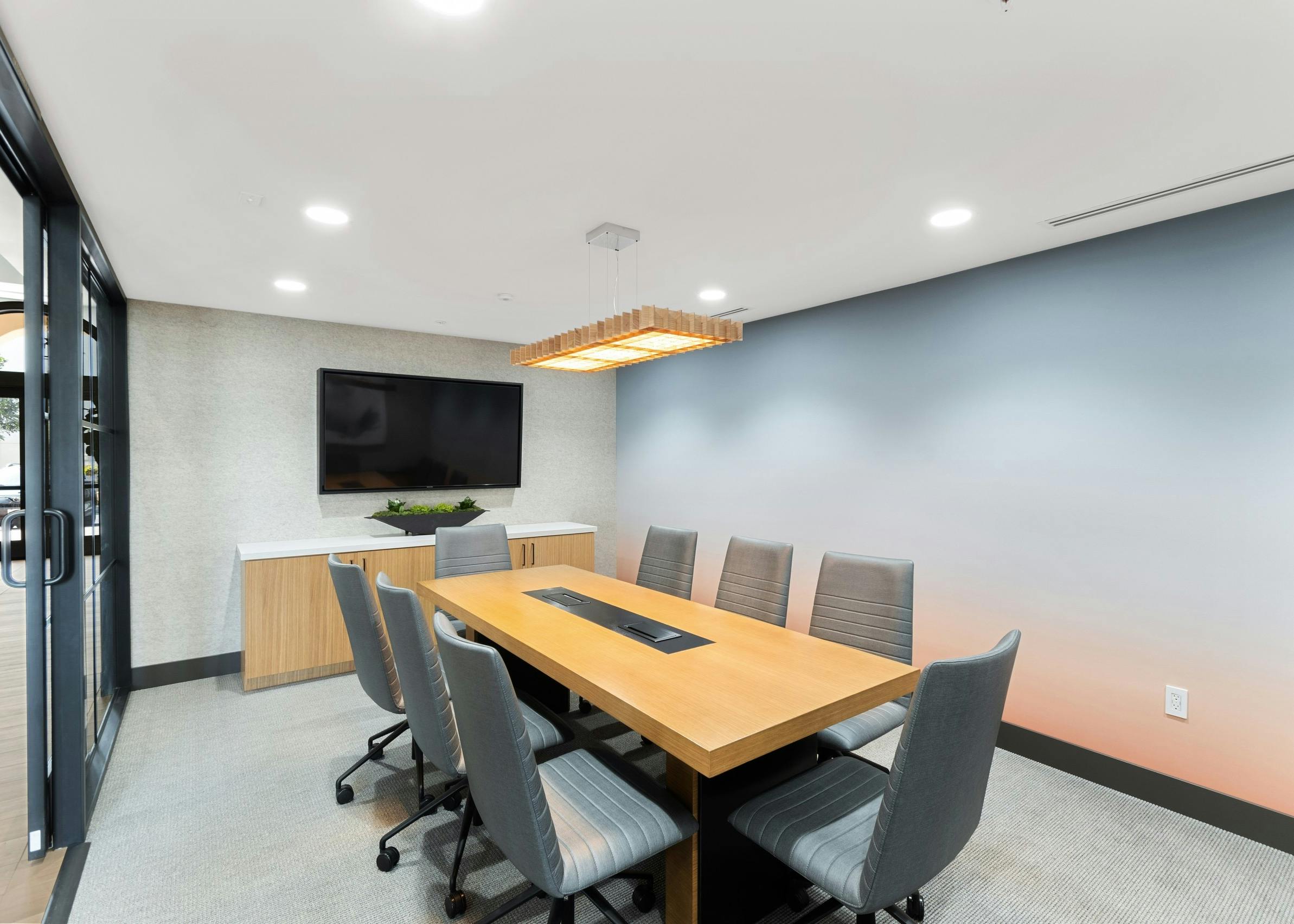 Conference room with large wooden table and gray chairs and big screen TV at AMLI Spanish Hills apartments