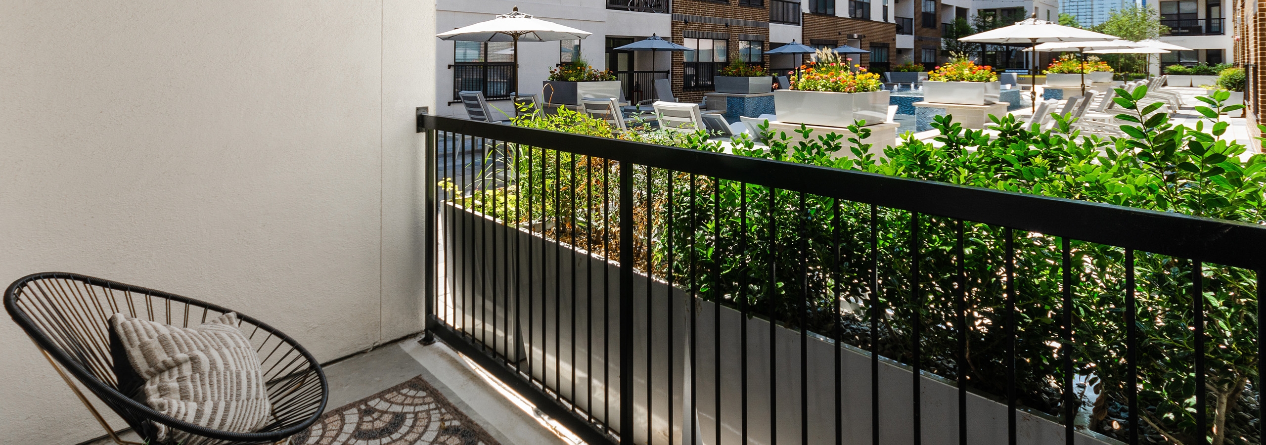 AMLI Quadrangle apartment patio with chair with pillow overlooking landscaped courtyard with cooling spa and lounge seating